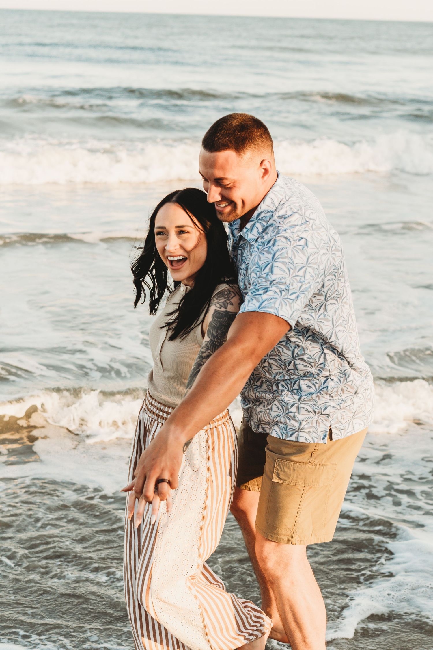 Laughing couple playing in ocean waves on sunny beach day.