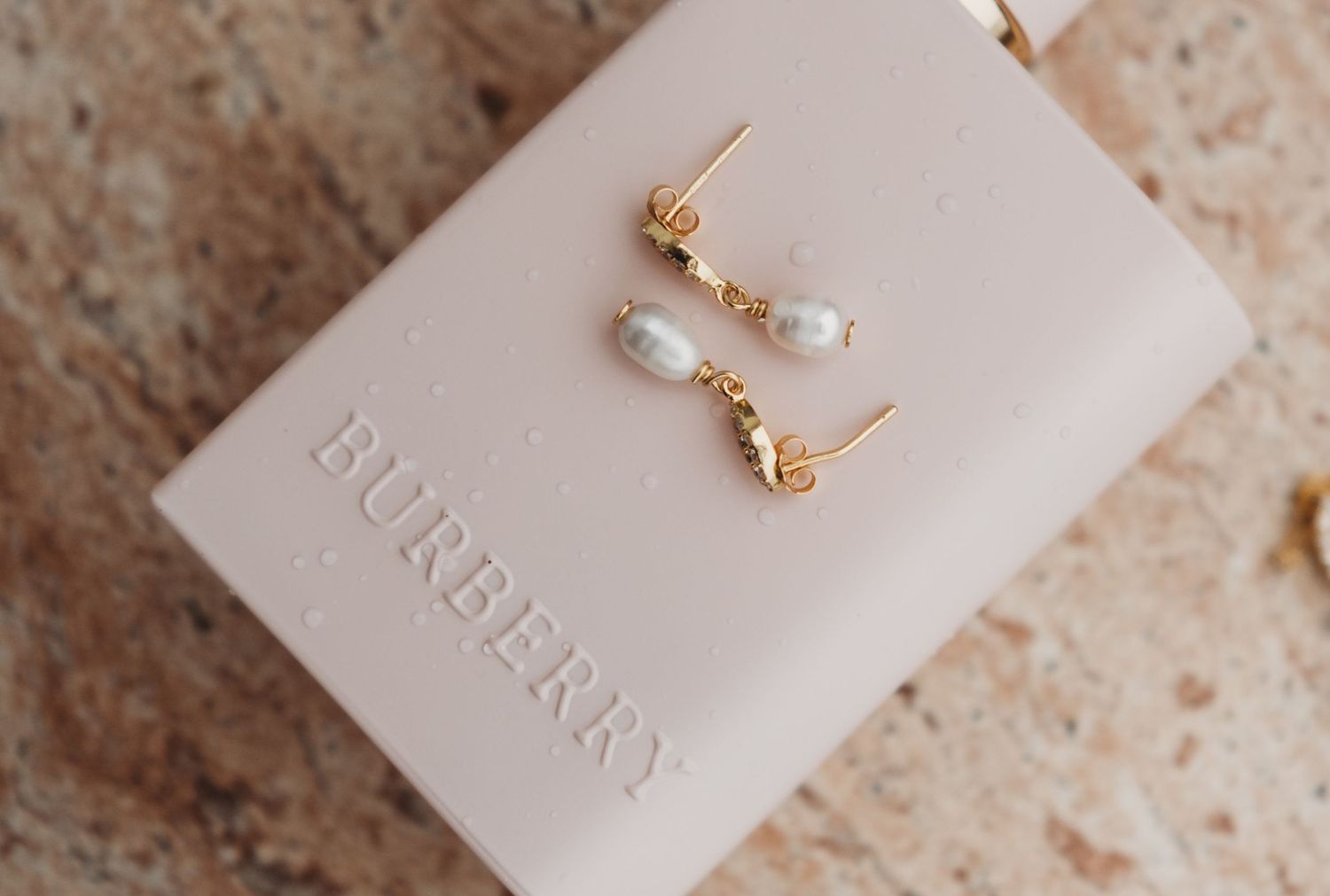 Delicate gold drop earrings with freshwater pearls displayed on a pink Burberry box.