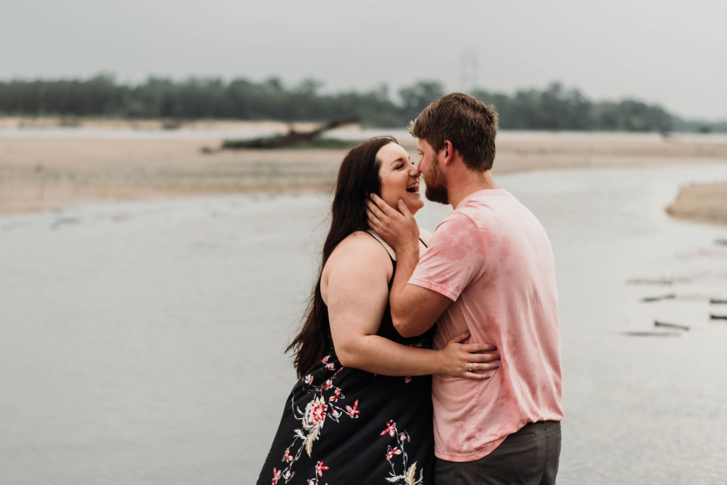 Couple sharing a romantic almost-kiss embrace on a cloudy beach shoreline during engagement photos.