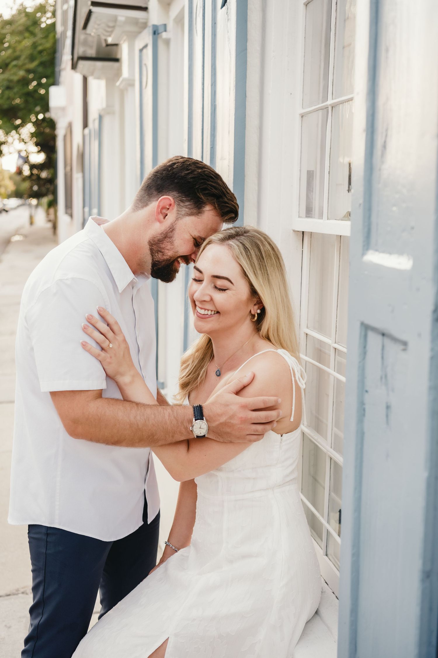 Smiling couple embracing tenderly against a blue building wall during a romantic outdoor engagement photo session.