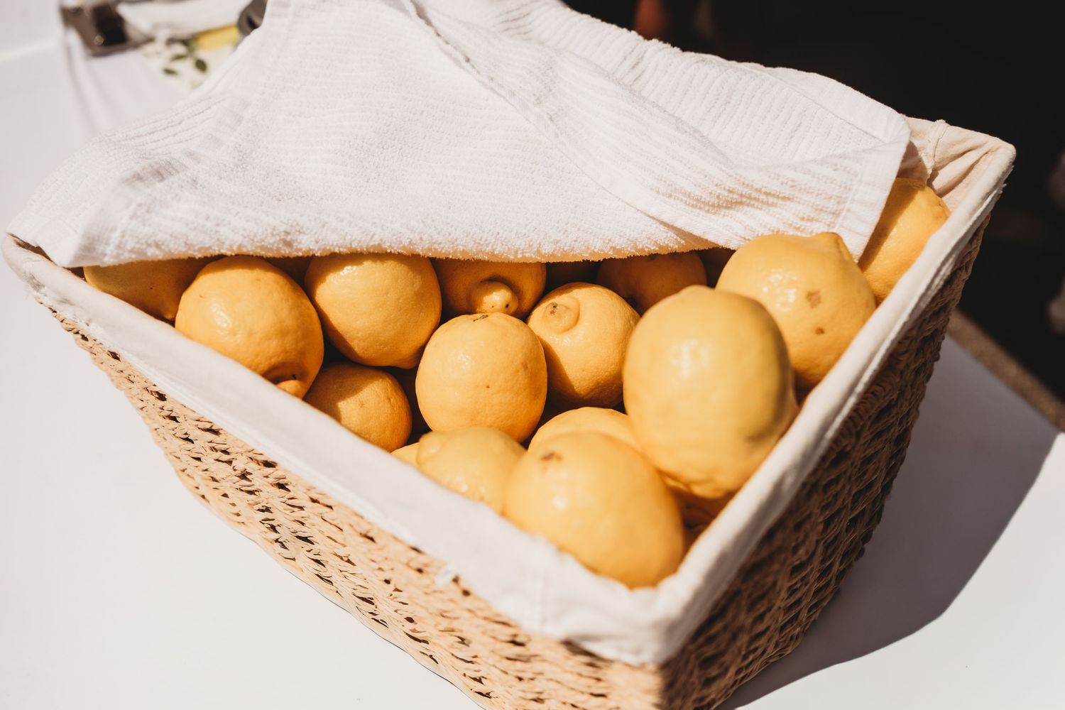 A wicker basket lined with white cloth filled with fresh yellow potatoes on a white table.