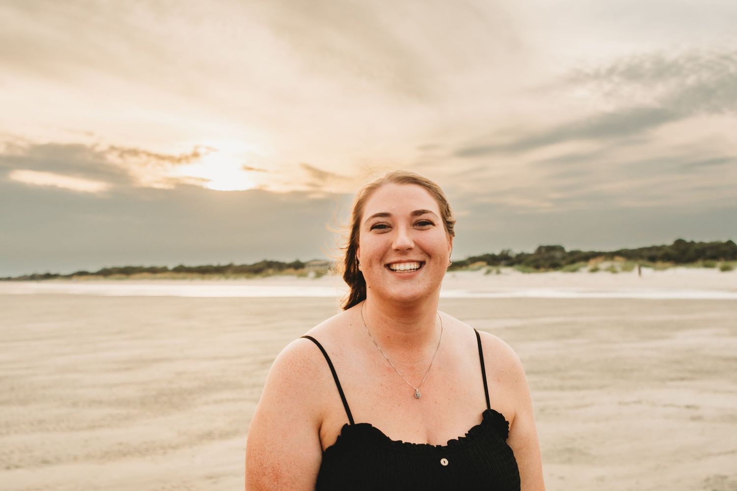 Smiling woman in black top standing on beach during golden sunset.