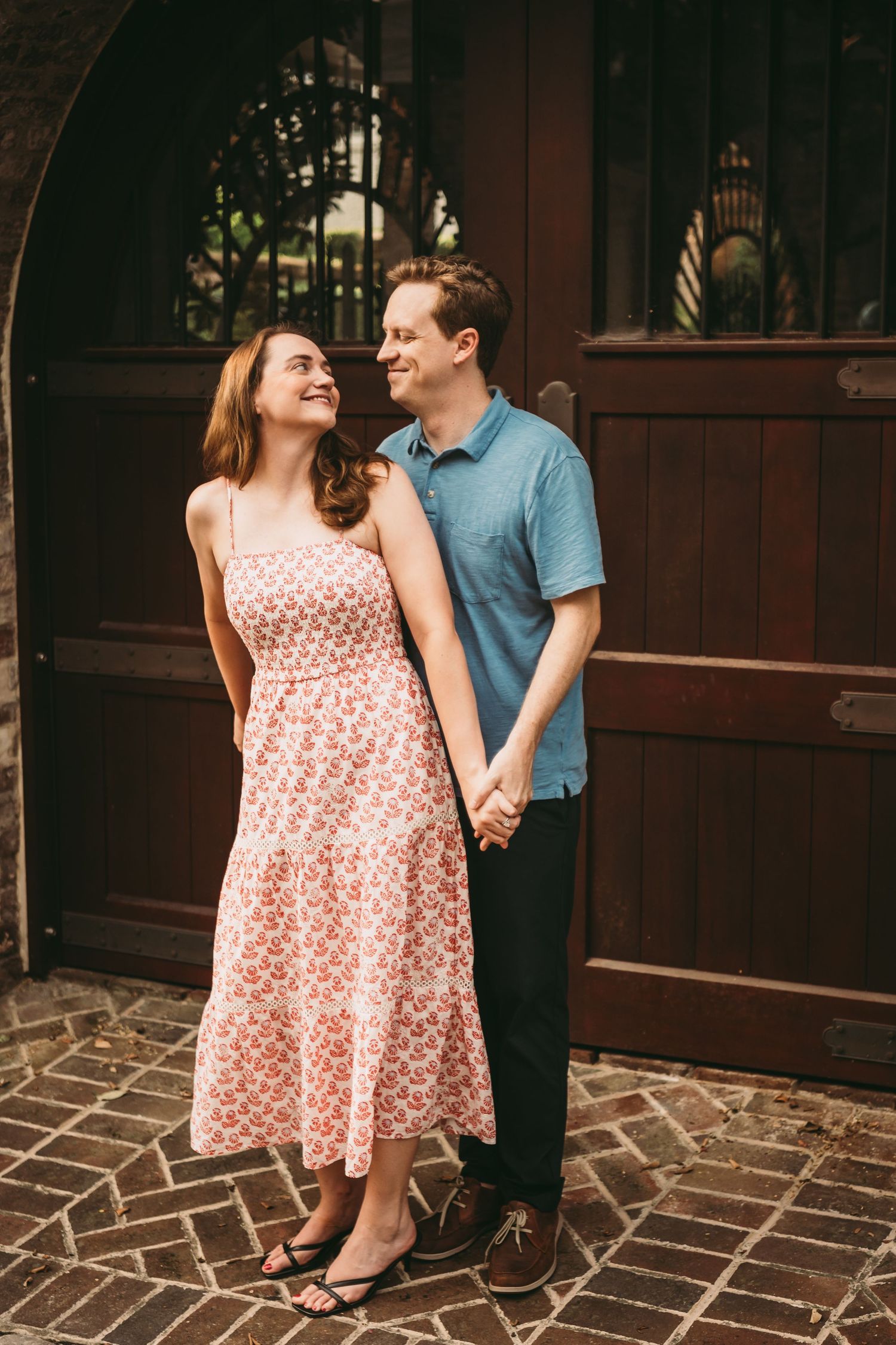 Couple holding hands and smiling at each other in front of wooden doors outdoors.
