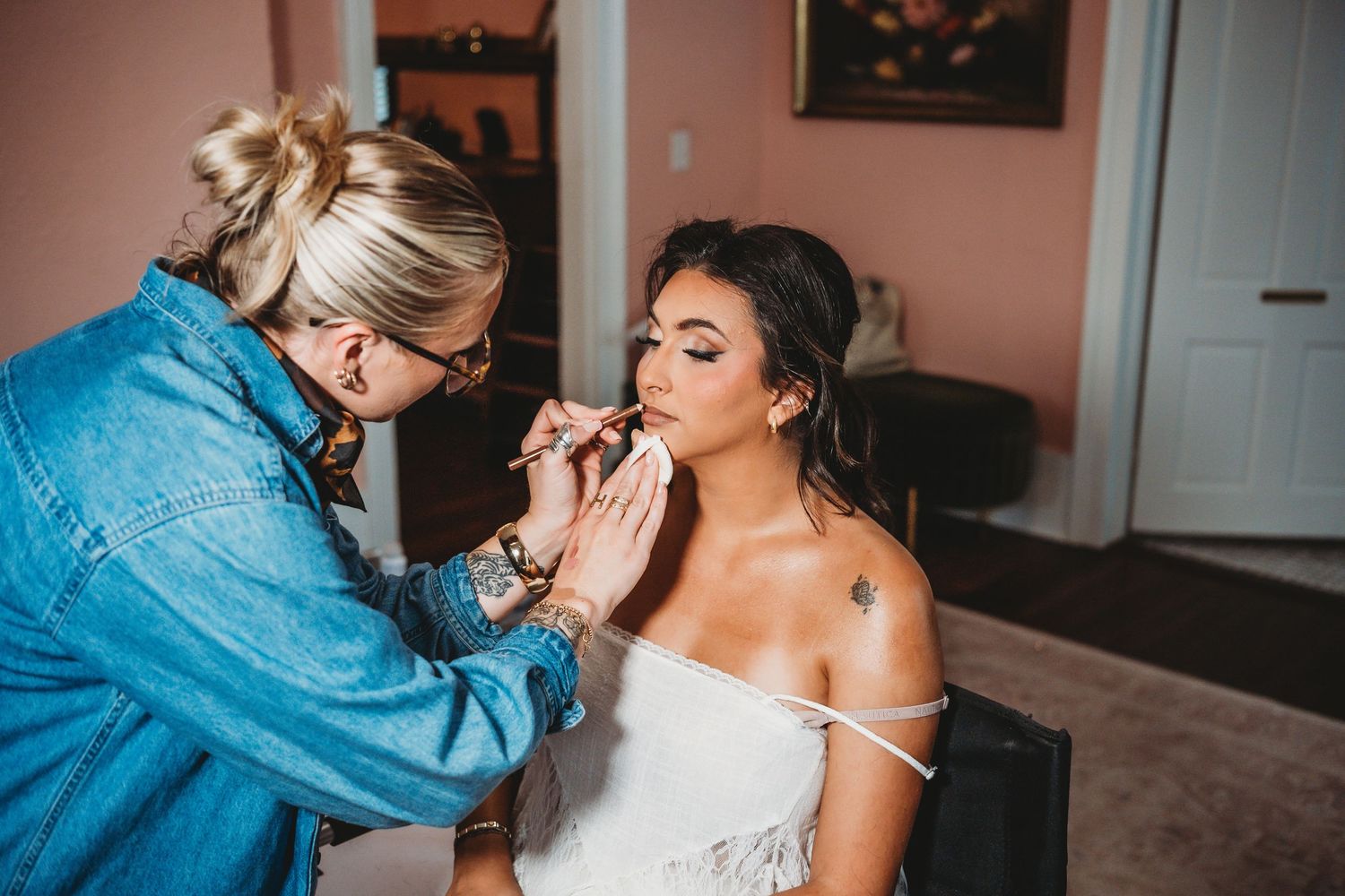 Makeup artist applying lipstick to bride in white dress before wedding.