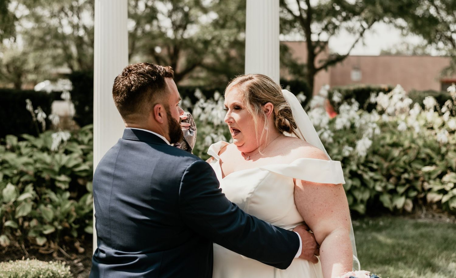Groom surprises bride with cake smash at outdoor garden wedding ceremony.