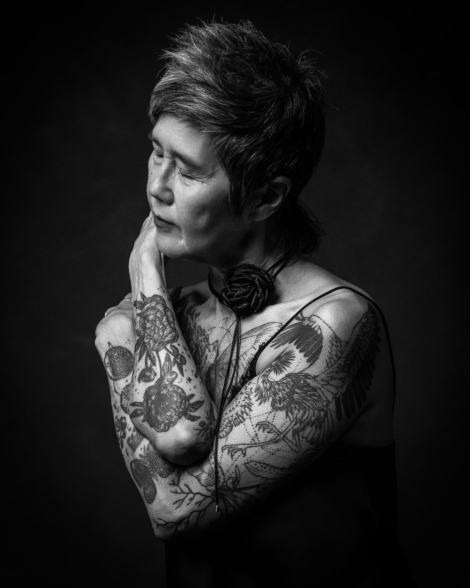 Black and white portrait of a woman with short hair and extensive floral tattoos on arms and chest.