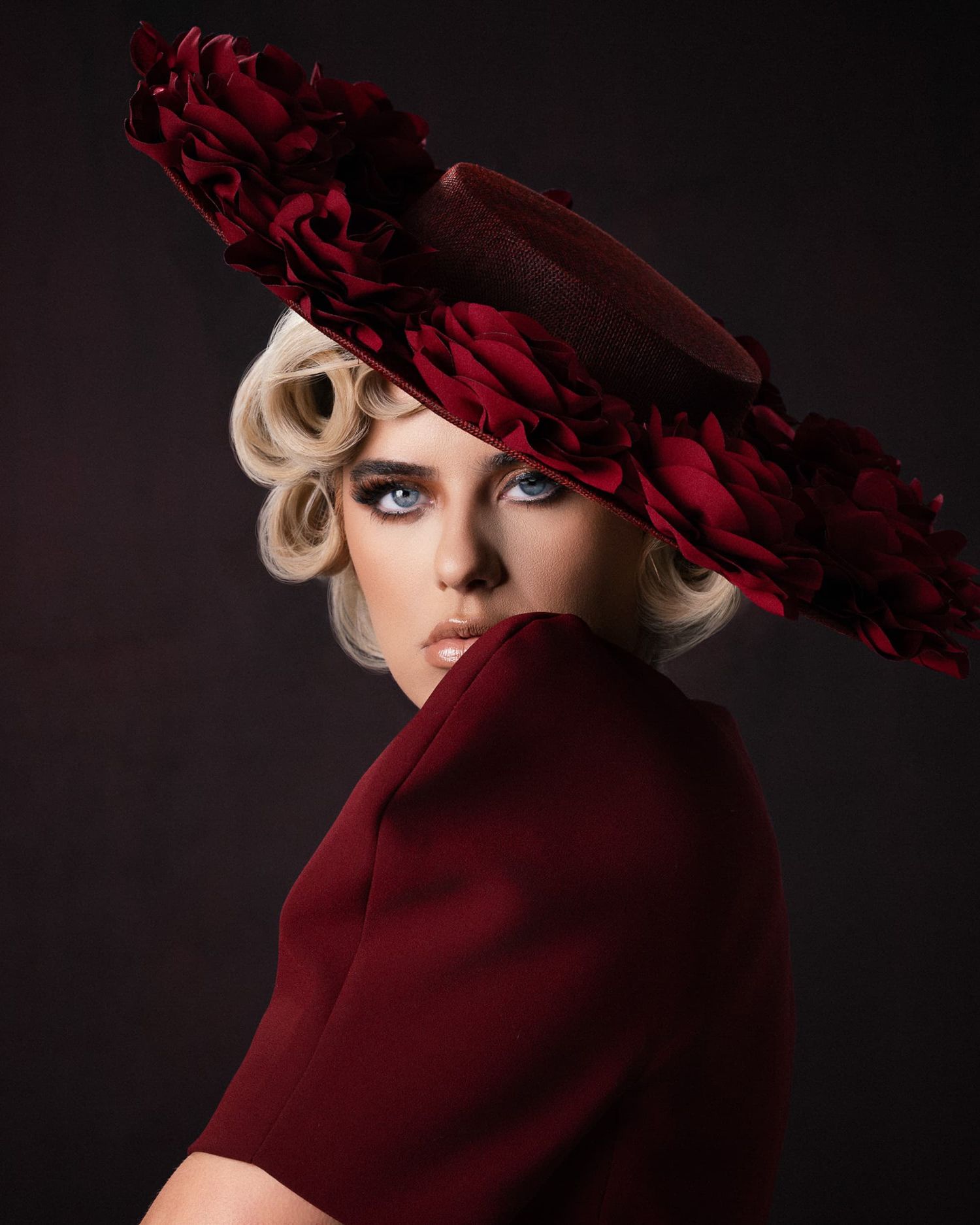 Blonde model in burgundy outfit wearing a large floral wide-brim hat.