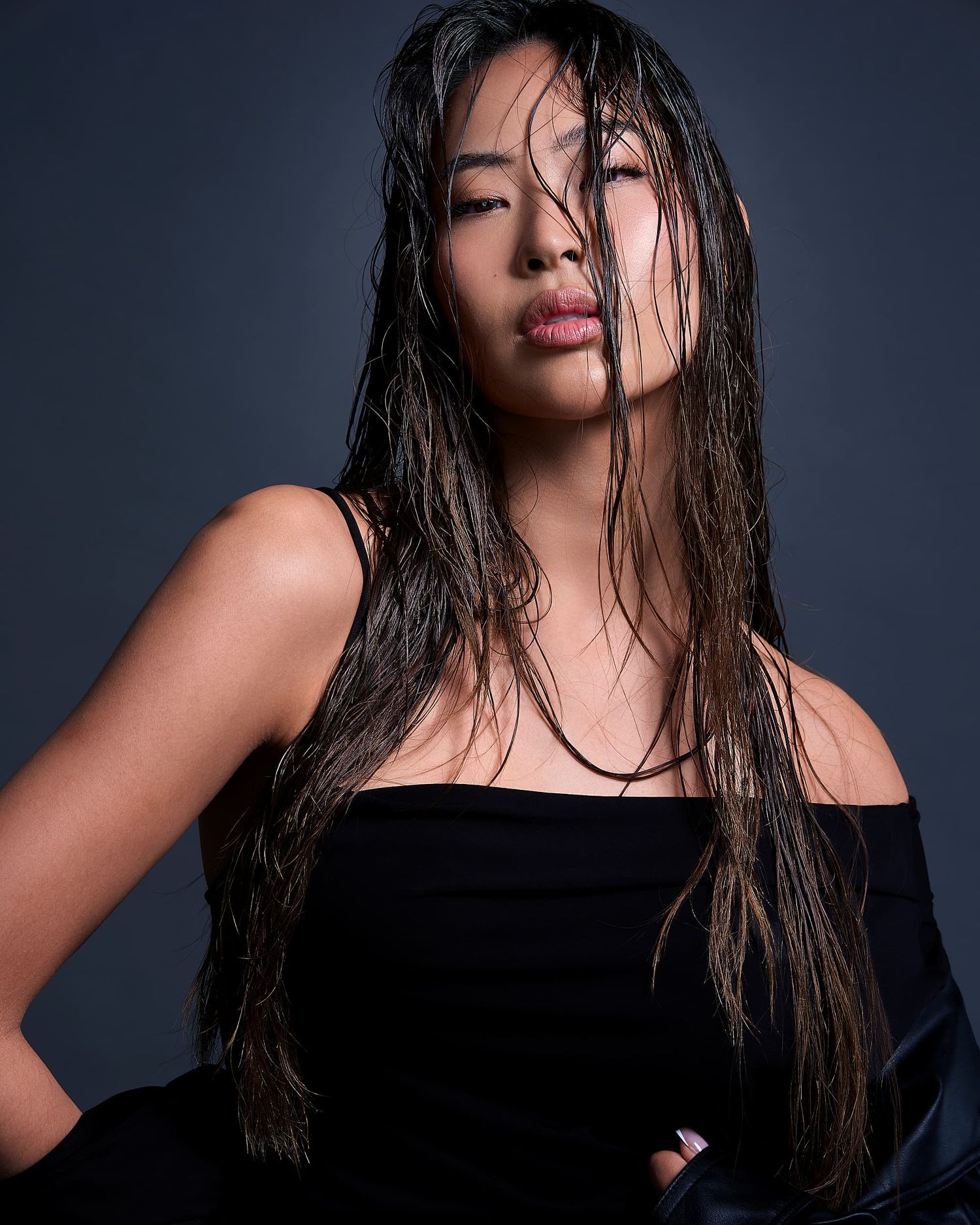 Woman in black off-shoulder top with wet hair posing dramatically against dark studio background.