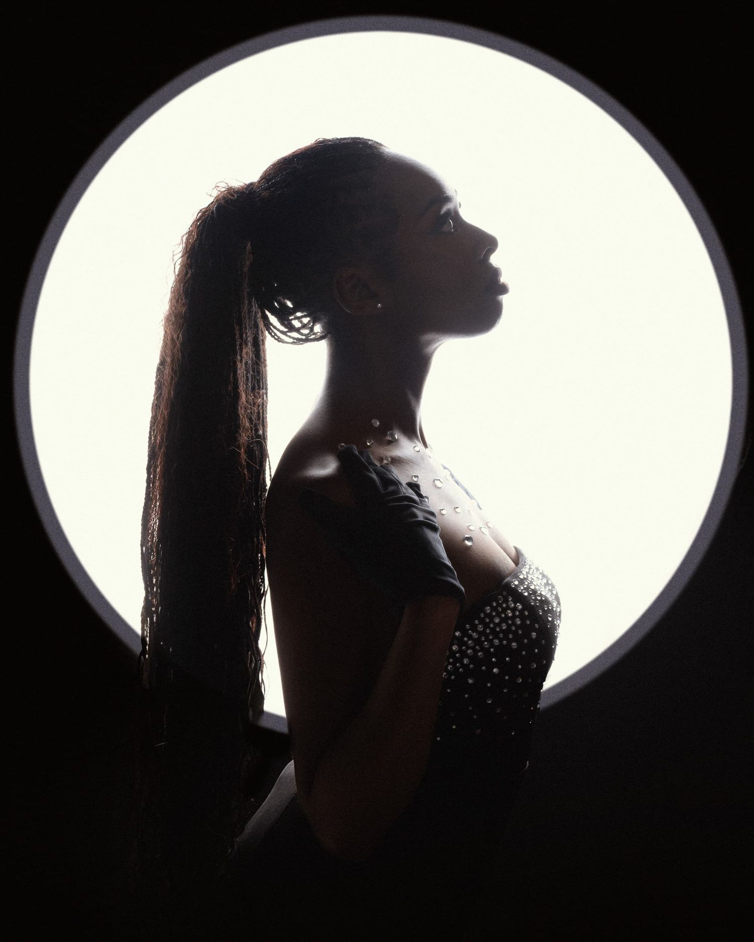 Silhouette of a woman with a long ponytail posed against a bright circular backlit background.