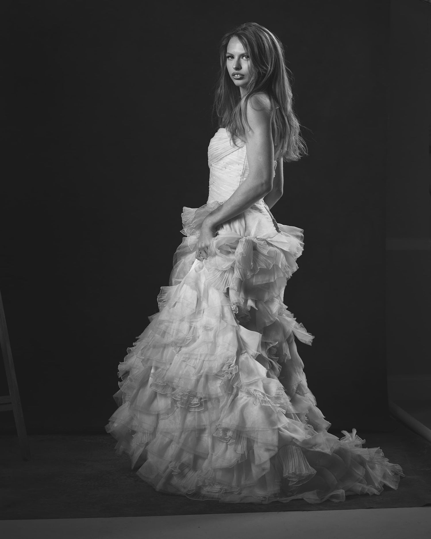Black and white photo of a model in a strapless ruffled wedding gown posing elegantly.