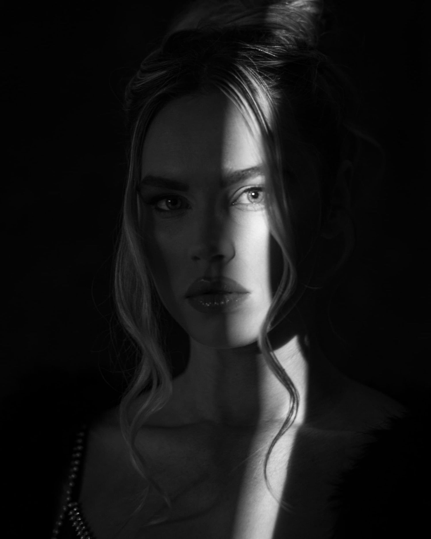 Striking black and white portrait of a blonde woman with light illuminating one side of her face.