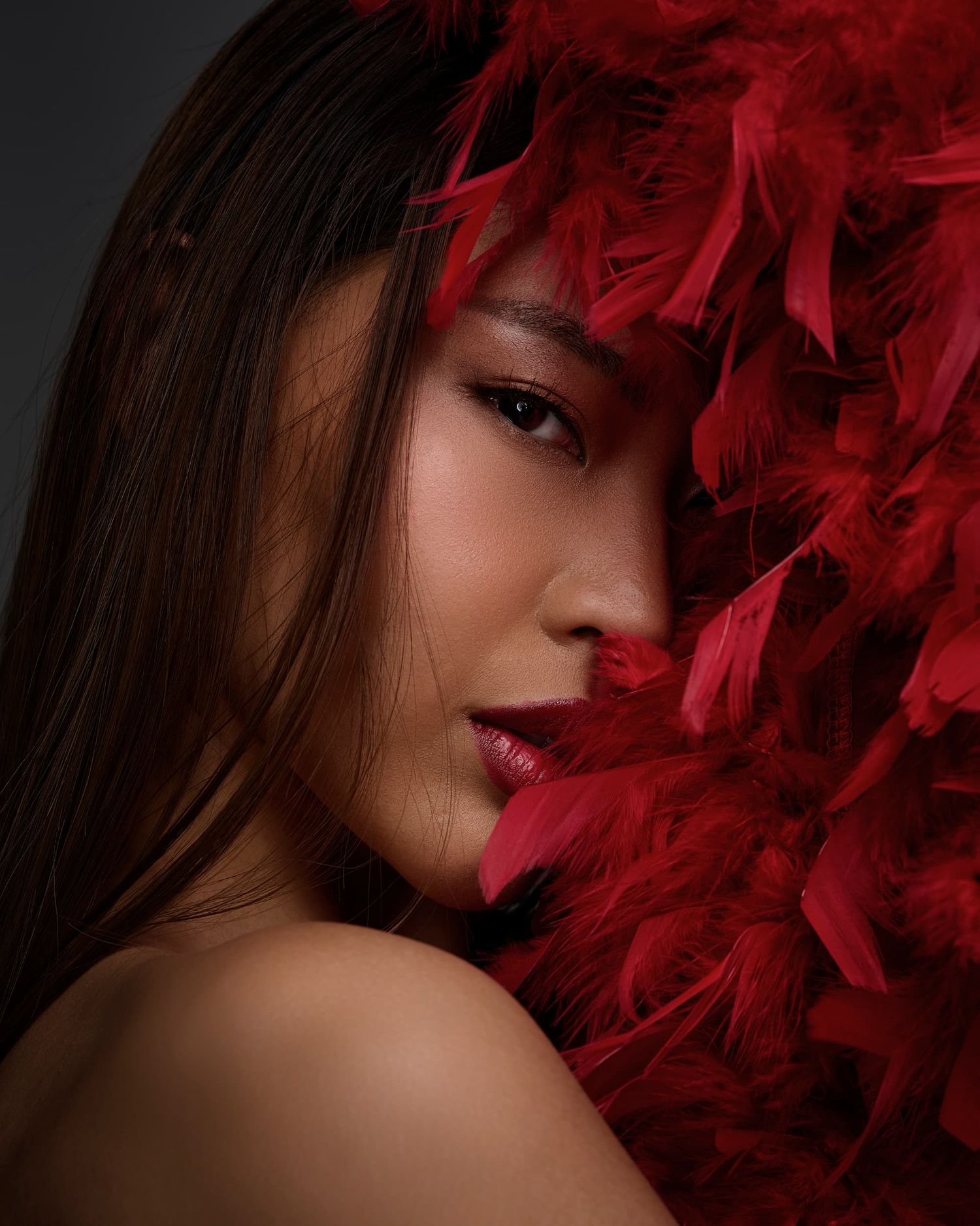 Woman with vibrant red feathers framing her face and bare shoulder.