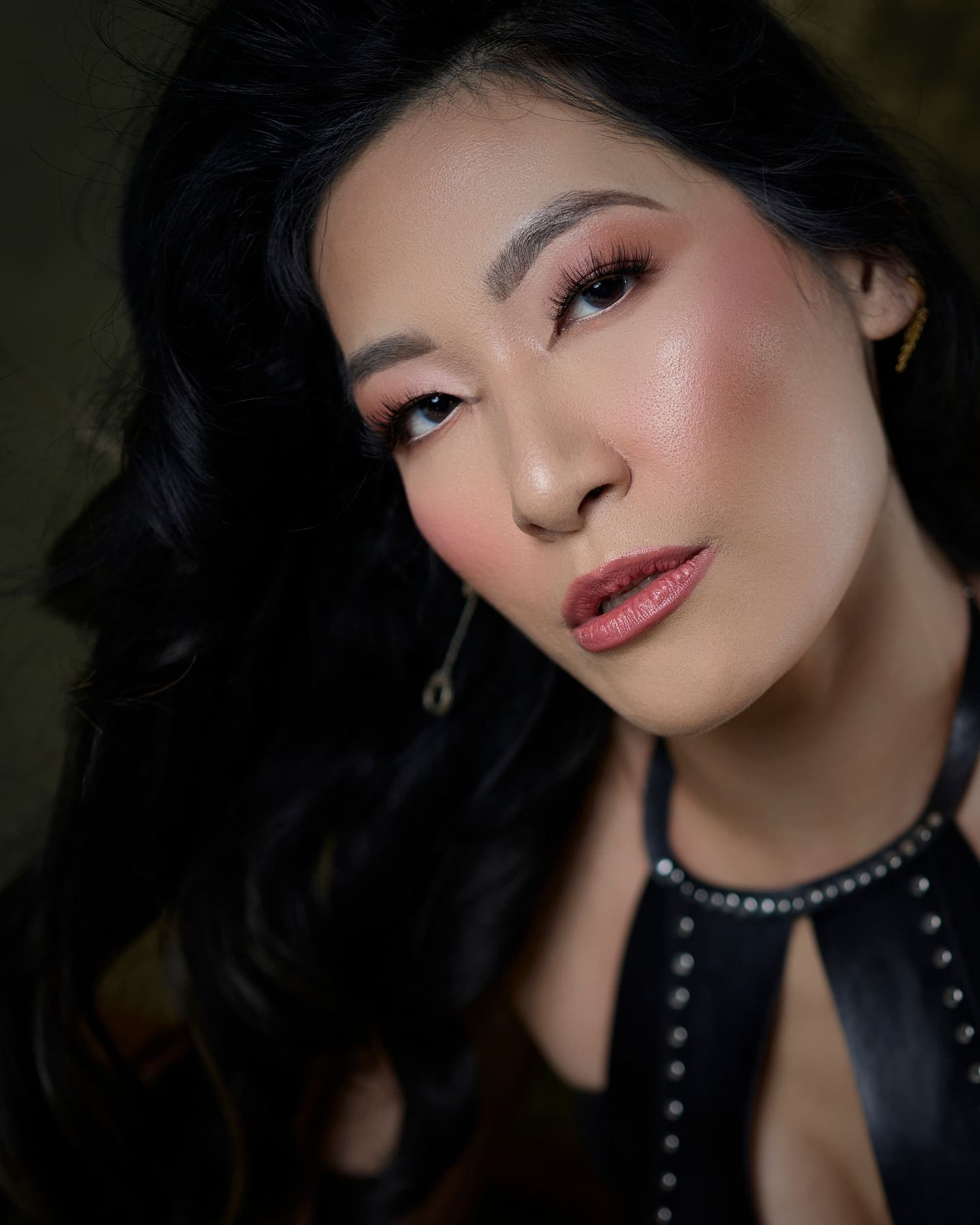 Close-up portrait of woman with black wavy hair and glowing warm makeup.