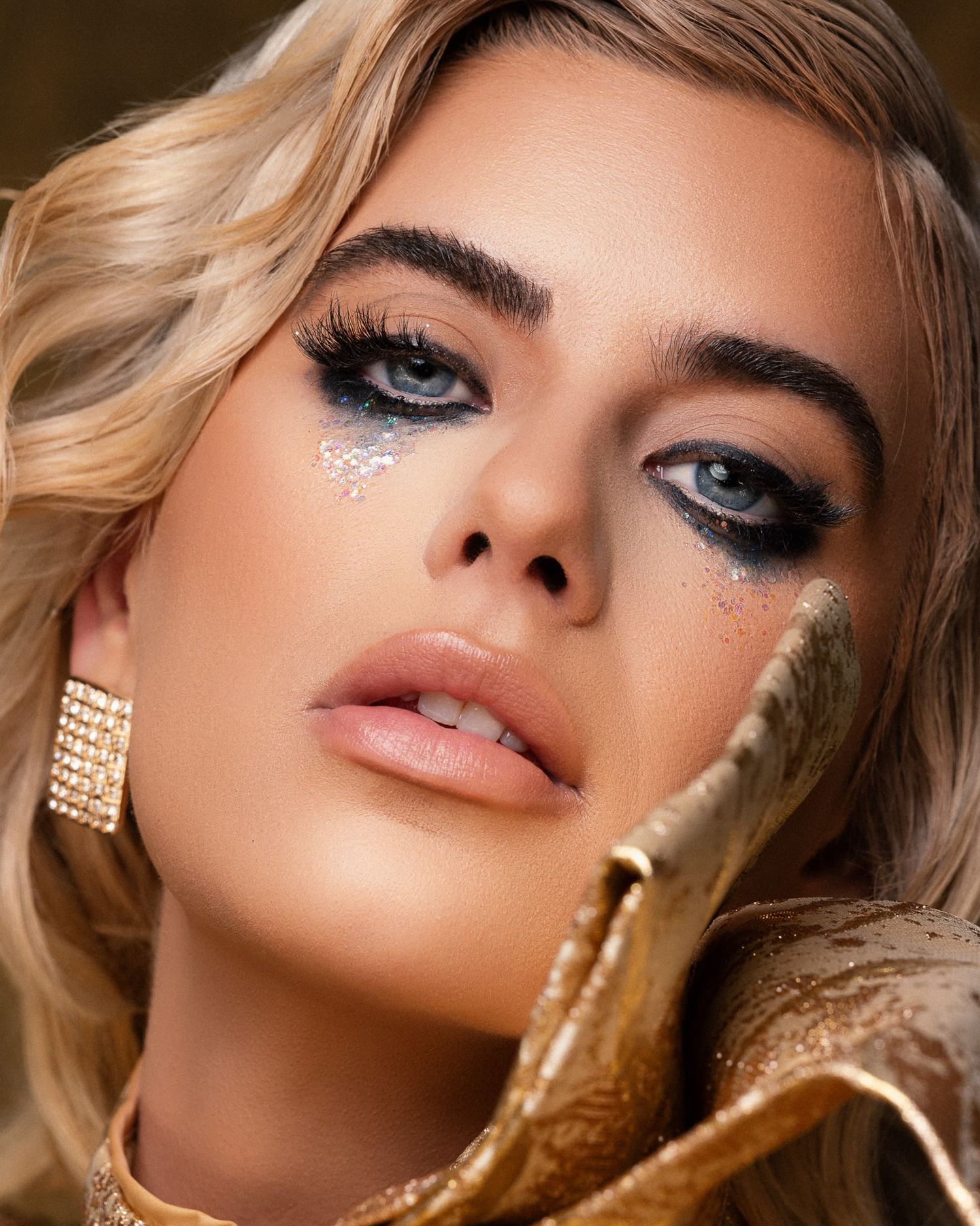 Close-up of a blonde model with dramatic smoky eye makeup and glitter tears.