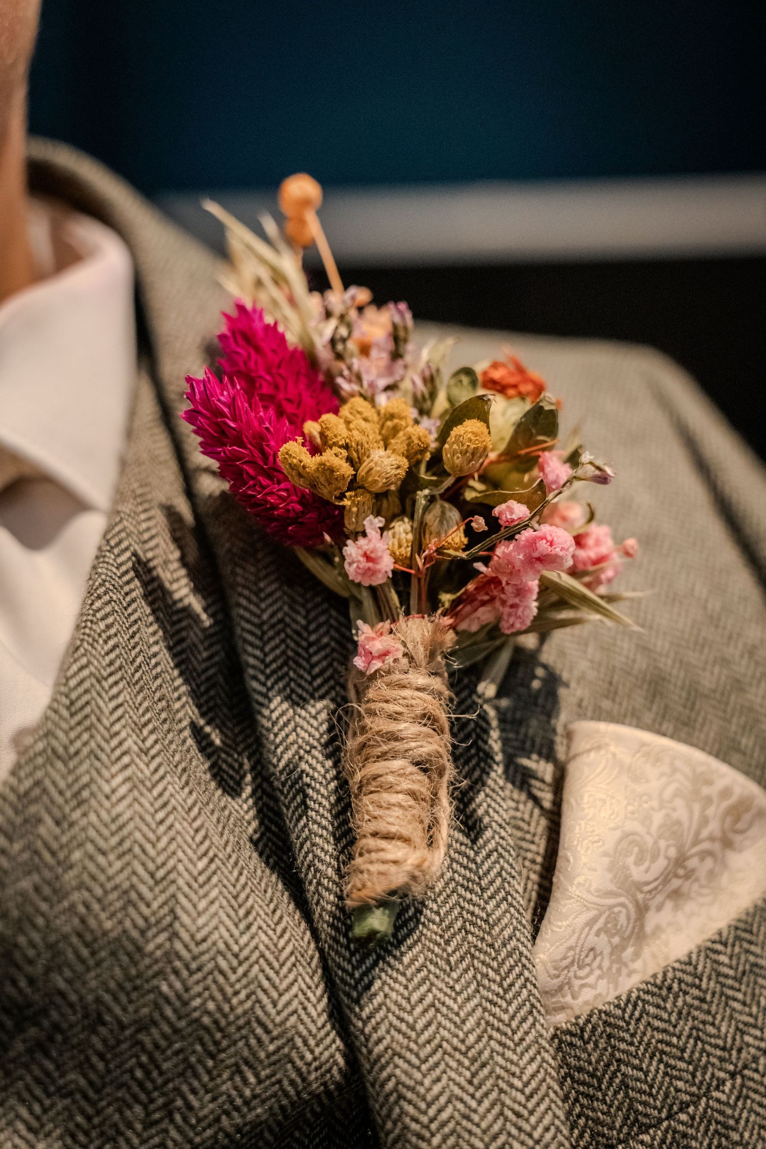 Close-up of a colourful dried-flower buttonhole pinned to a groom’s grey herringbone wedding suit.