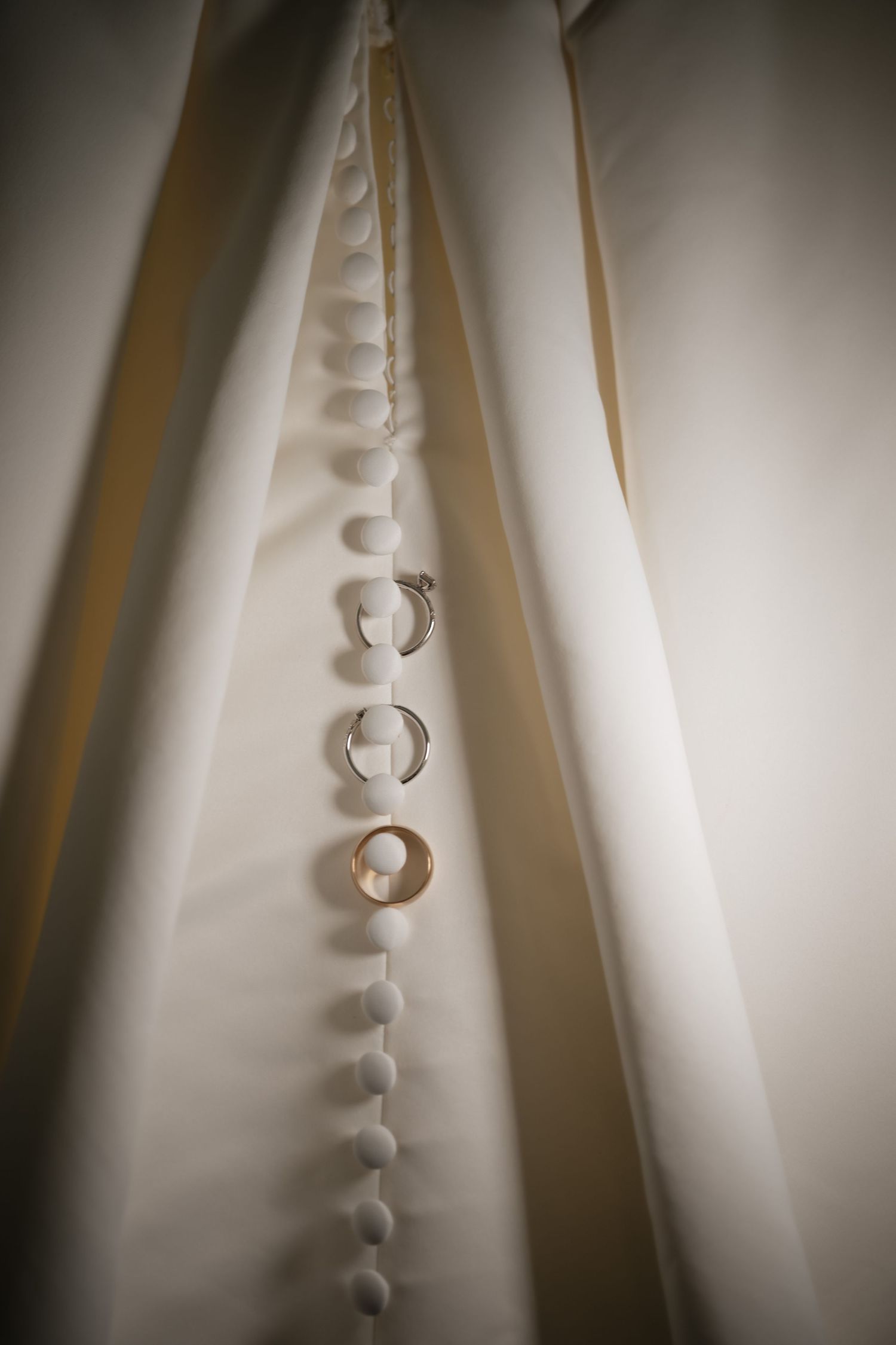 Wedding rings elegantly displayed on white dress buttons, showcasing delicate gold and silver bands.