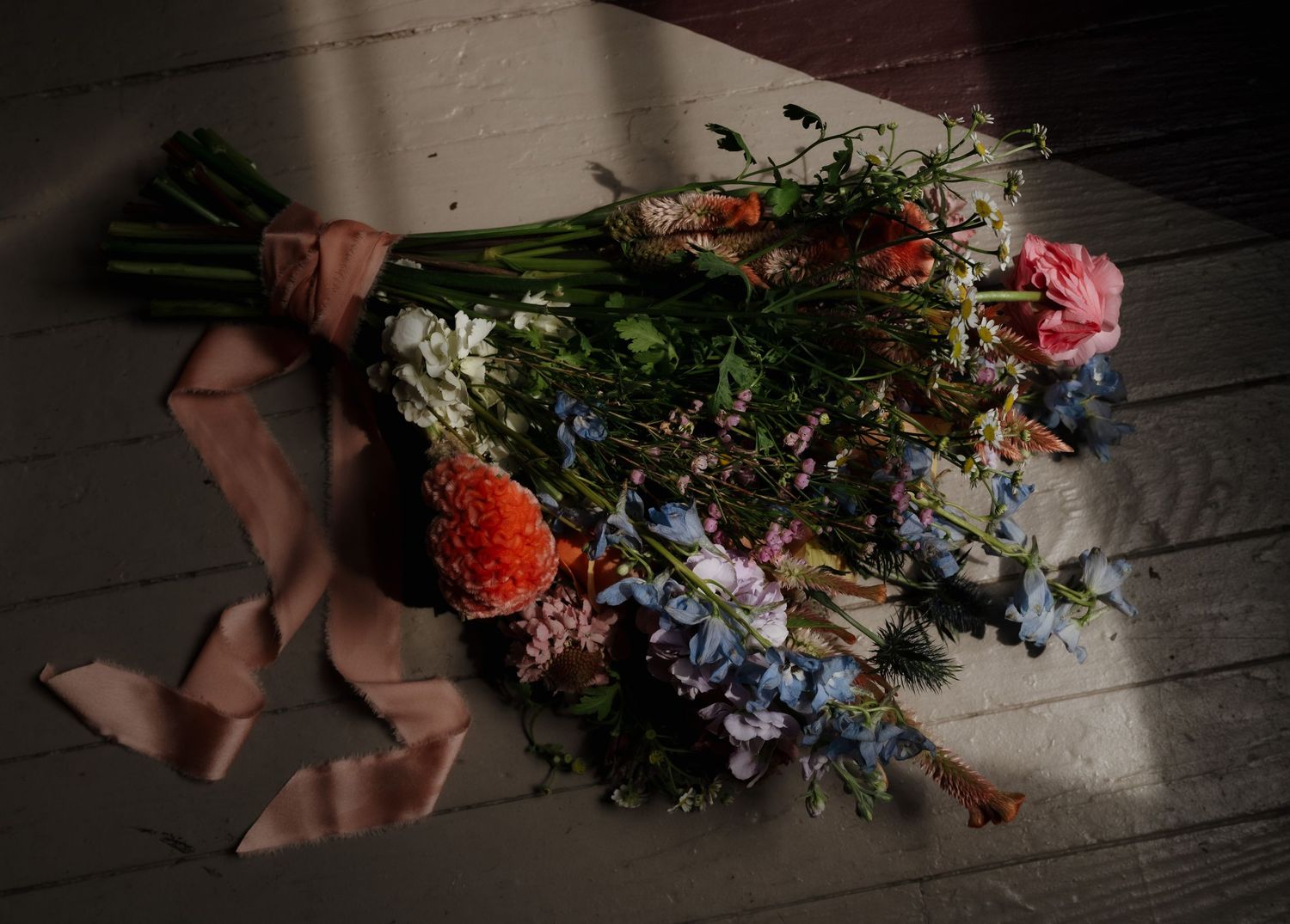 Delicate floral arrangements and bouquets being styled on a rustic wooden floor with visible hands working.