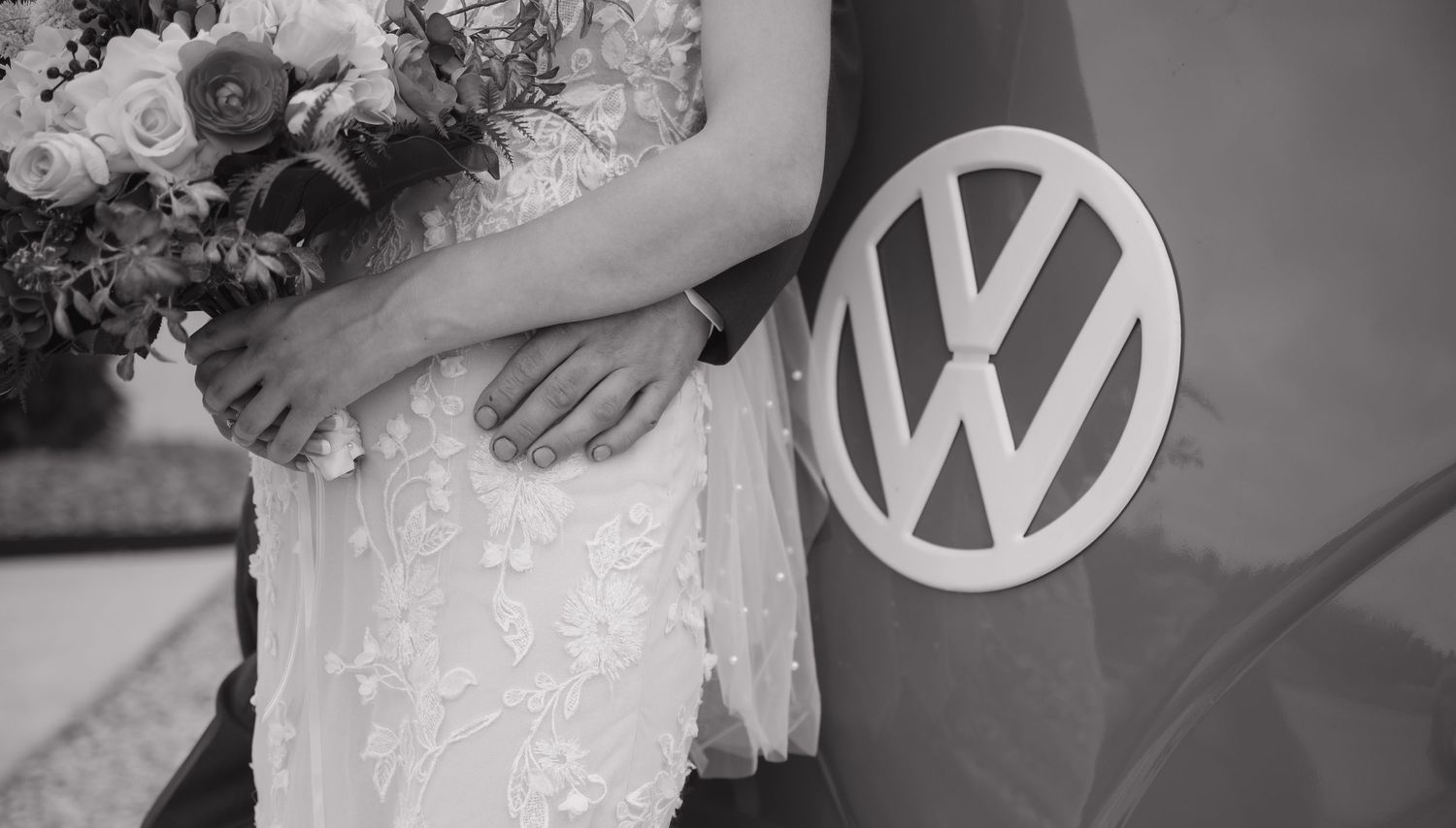 Black and white wedding photo of couple in lace dress holding bouquet beside a vintage Volkswagen van.