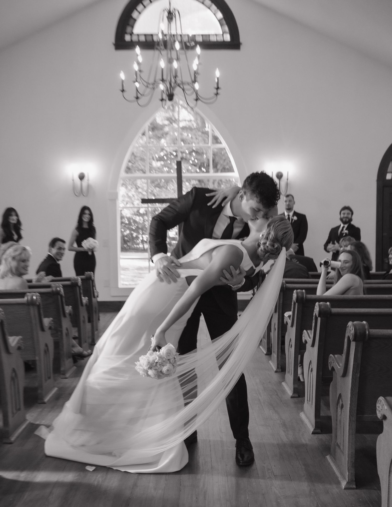 A romantic dip during a wedding ceremony in a chapel with arched windows and wooden pews.