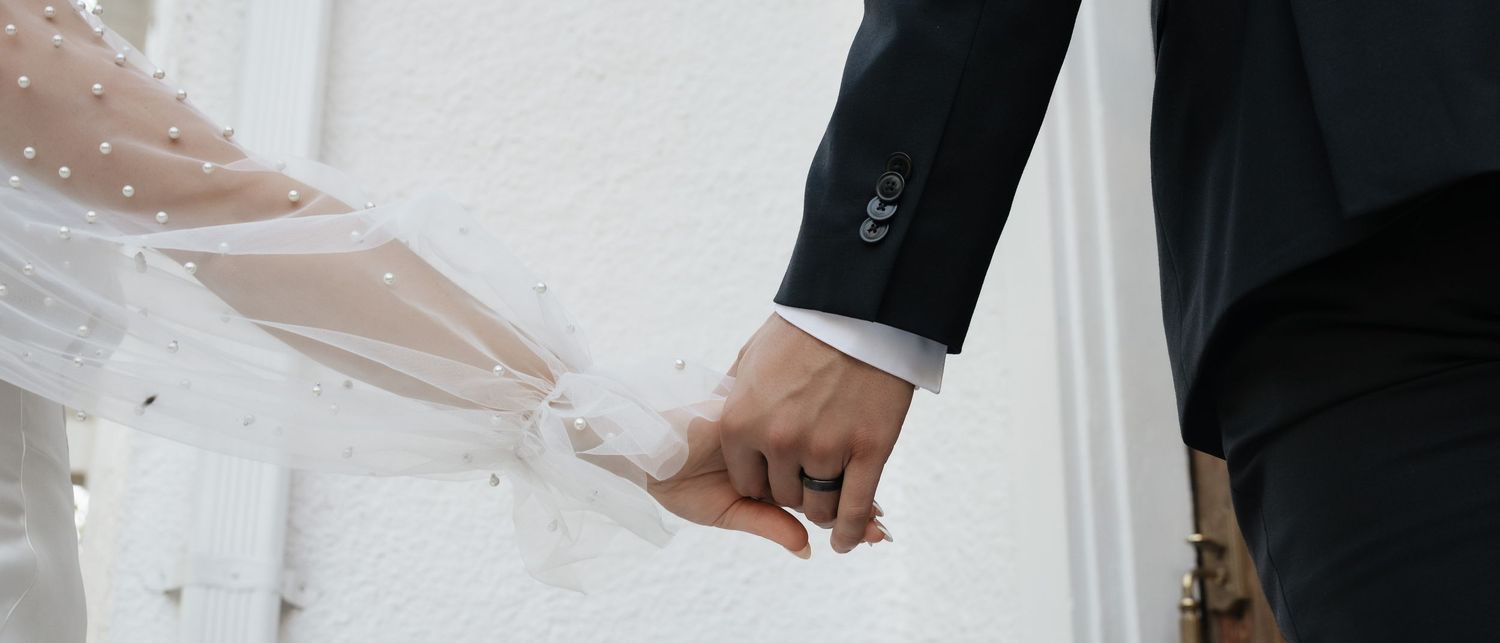 A close-up view of hands holding a white lace wedding dress against a bright background.
