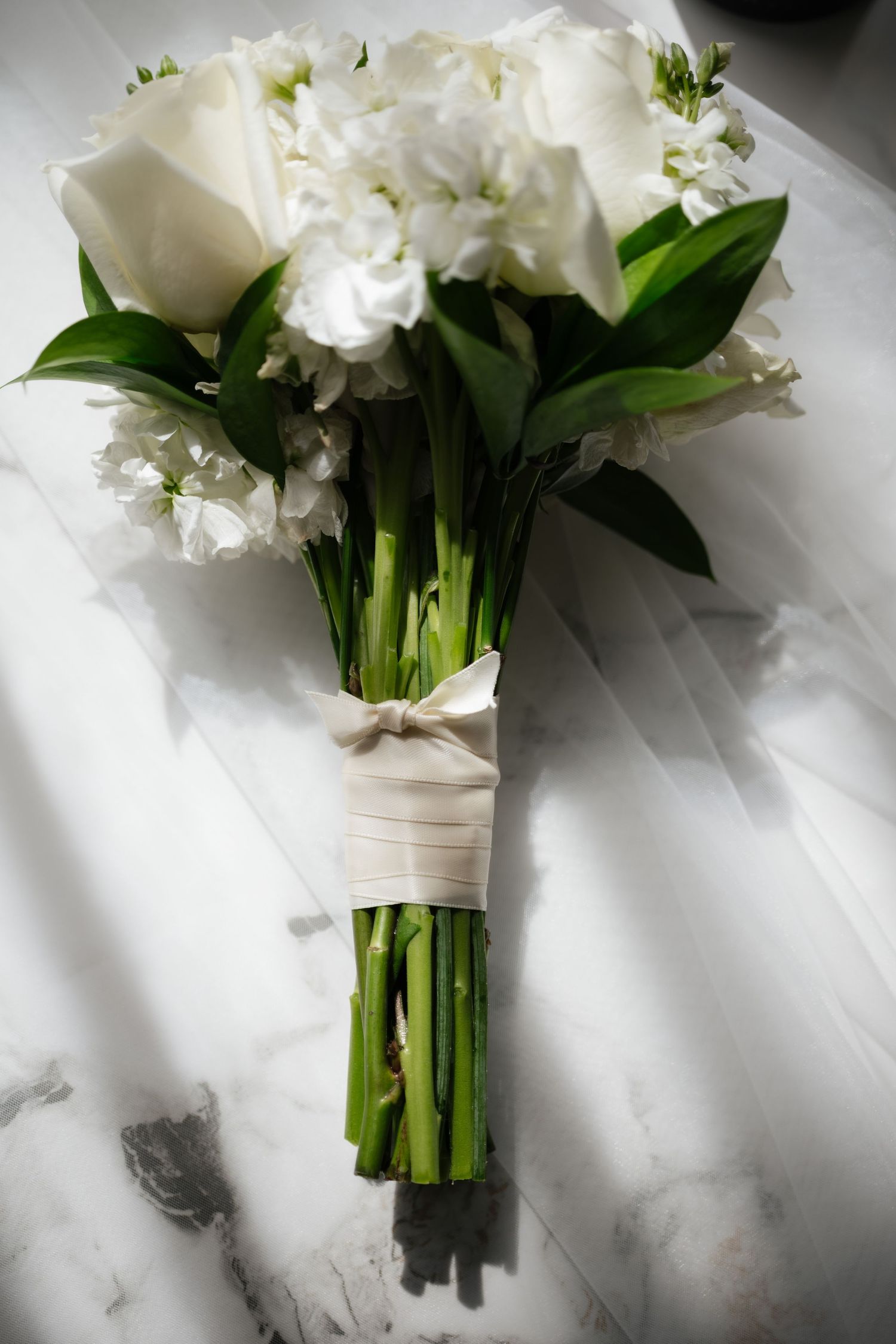 Classic bridal bouquet of white roses and hydrangeas tied with a satin ribbon on marble surface.