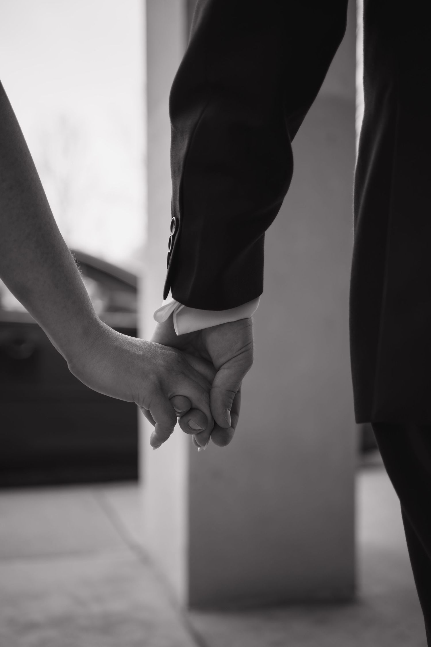 Close-up black and white photo of bride and groom holding hands during wedding ceremony.