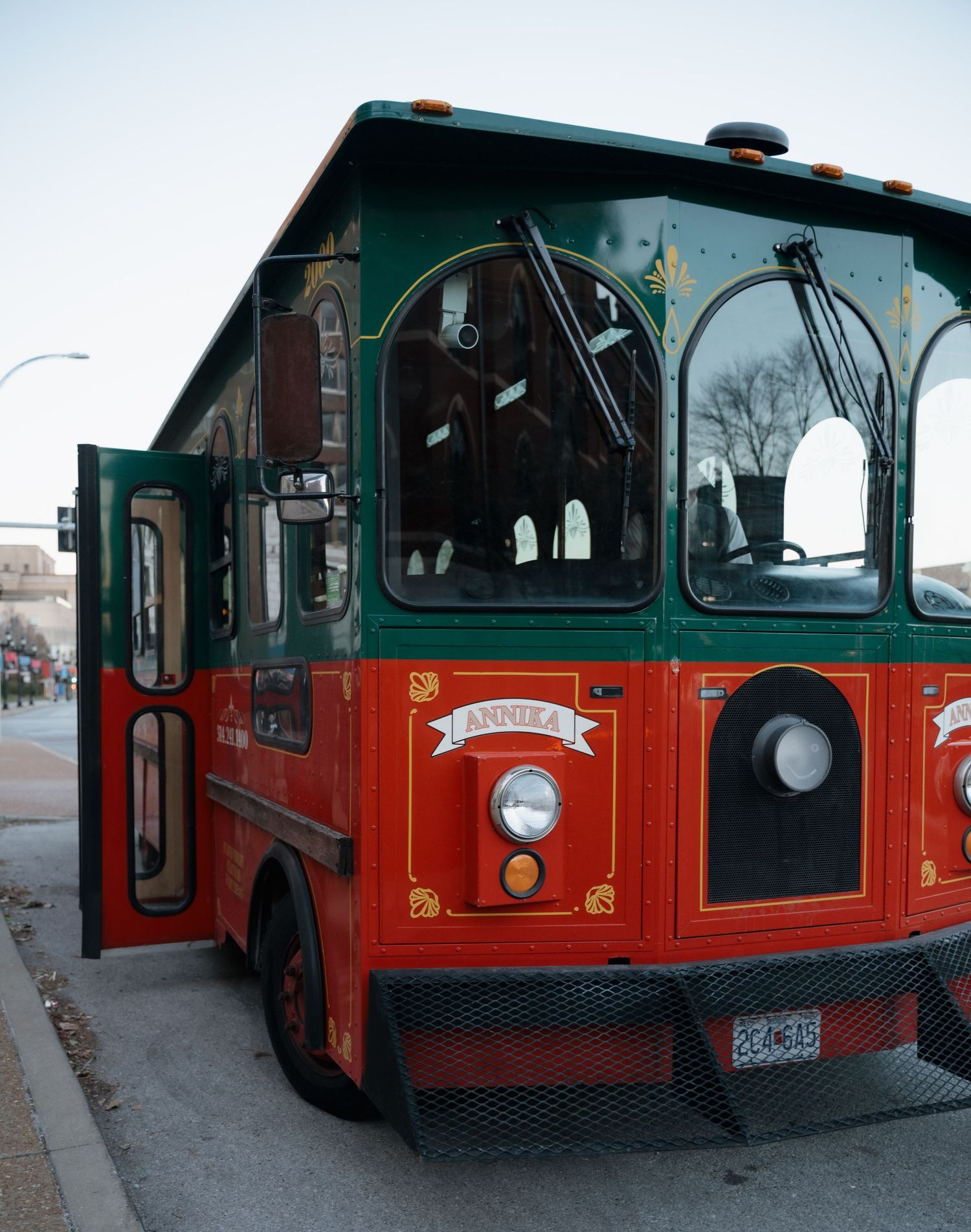 A vintage-style red and green trolley bus parked on a city street with decorative details and arched windows.