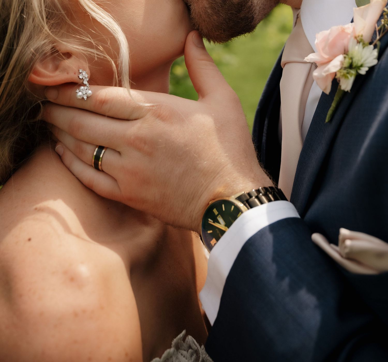 Close-up of bride and groom sharing a kiss, showcasing diamond ring and gold watch at wedding.