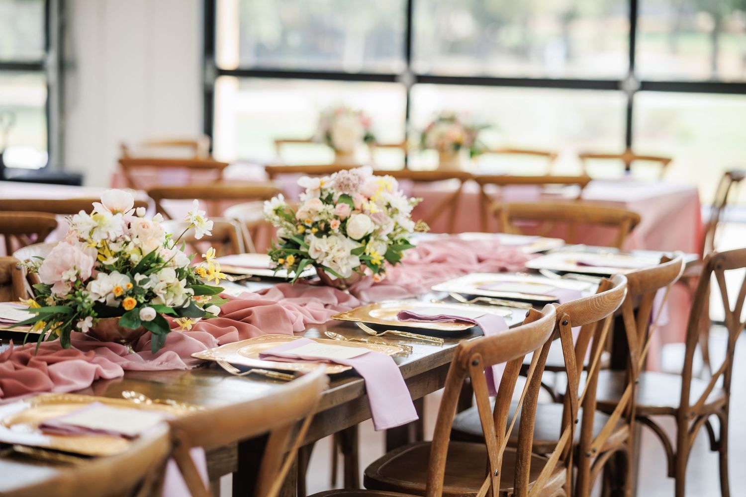 Elegant wedding reception table with floral centerpieces and wooden crossback chairs.