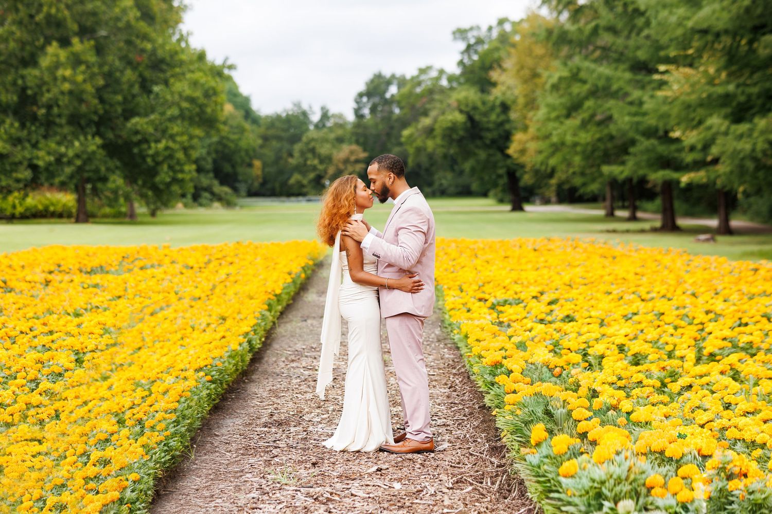 A couple embraces in a vibrant yellow sunflower field on a dirt path during a sunny summer day.