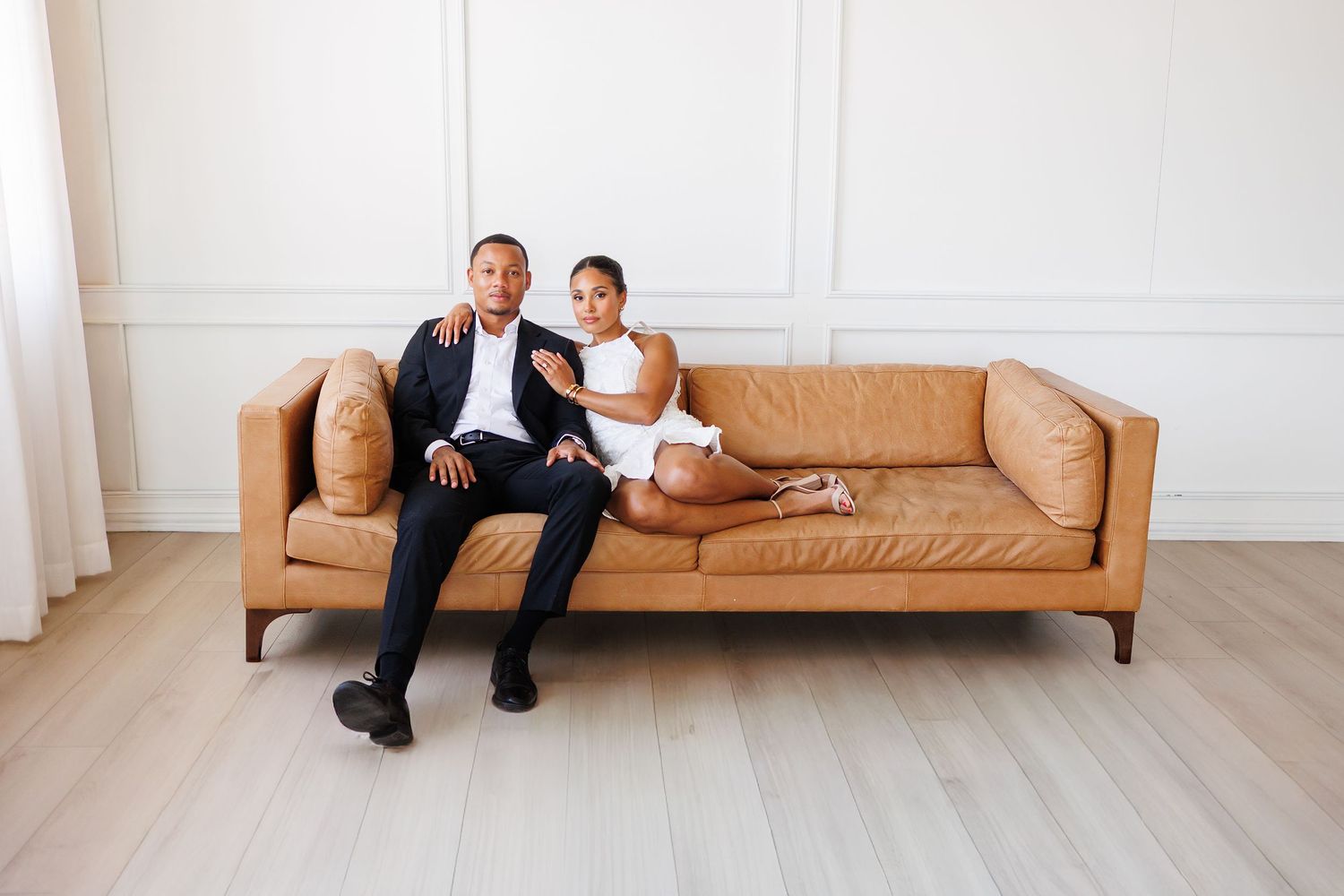 A person lounges on a tan leather sofa in a bright minimalist room with white walls and light wood flooring.