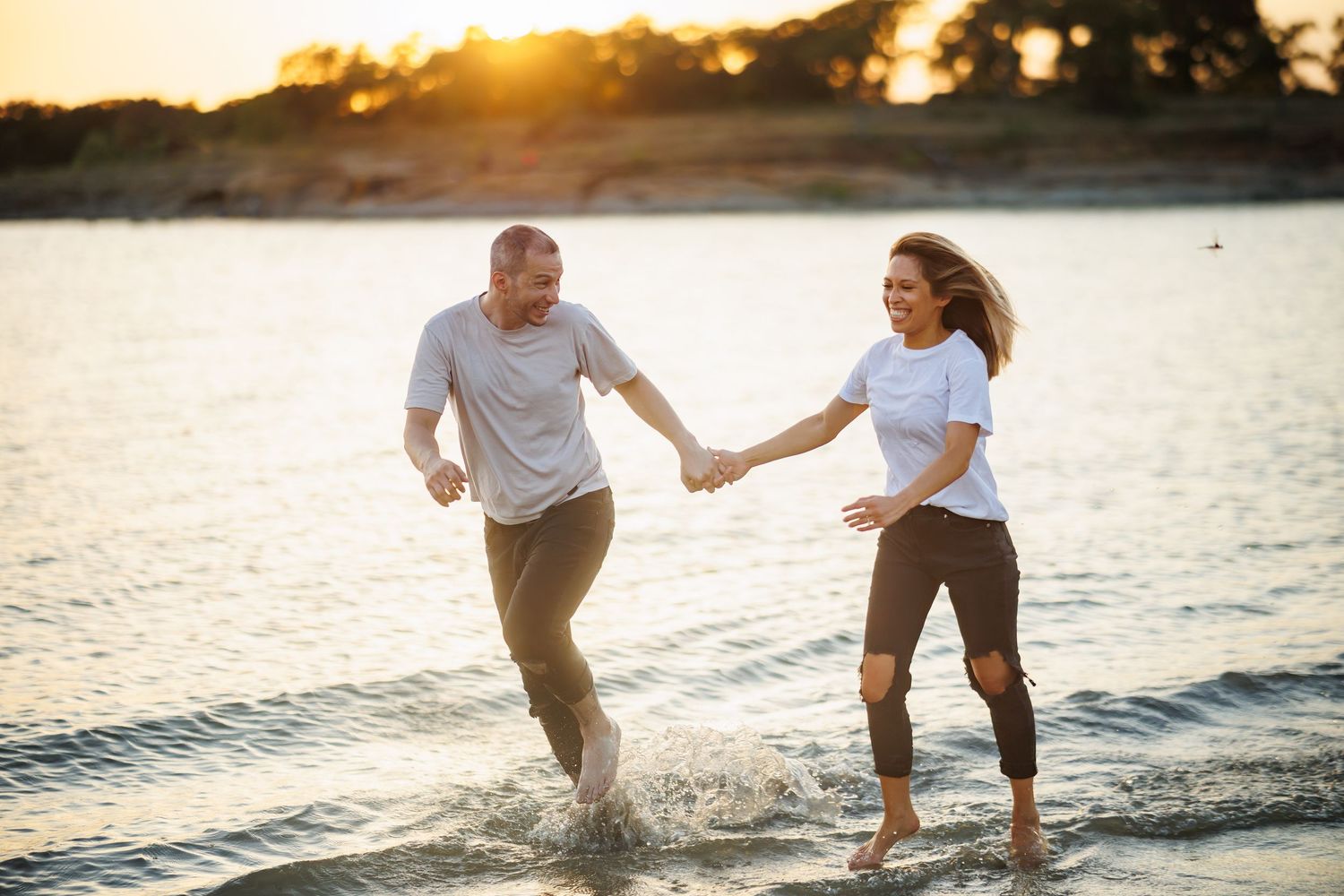 Couple splashing and running together along the beach shoreline at golden sunset.