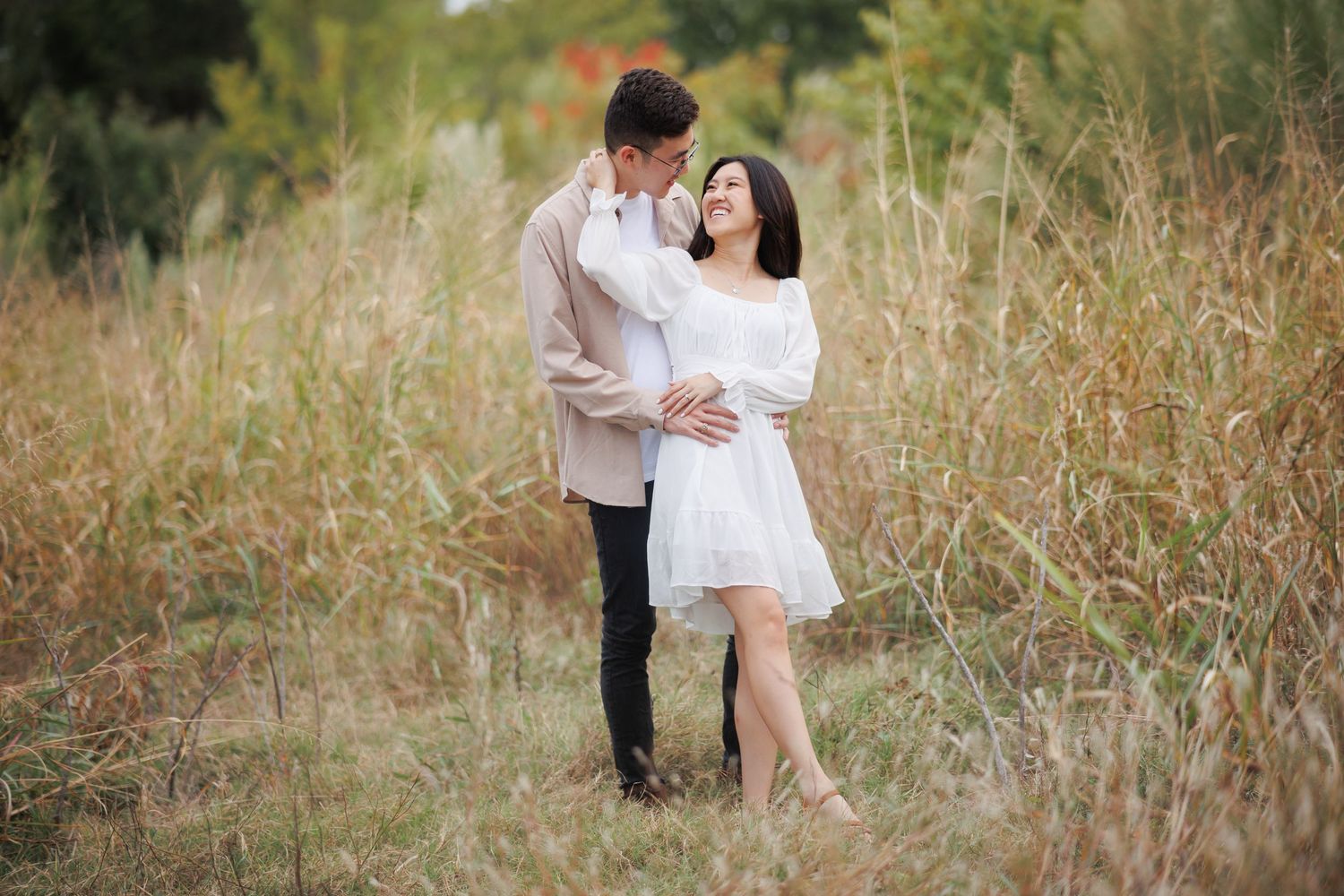 Romantic couple in white outfits embrace in a golden sunlit field during an outdoor photo session.