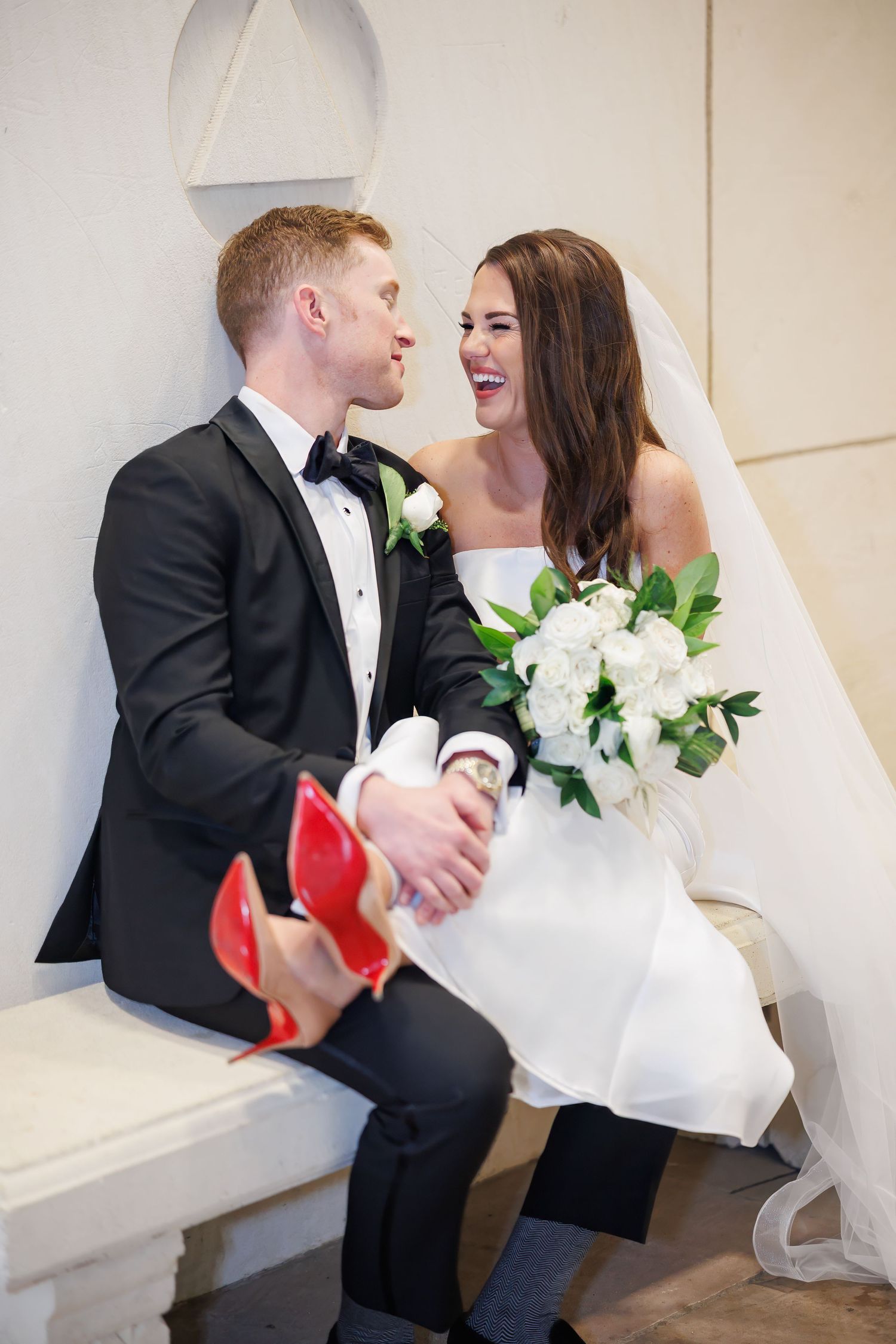 Newlyweds share a joyful moment together while showing off red-soled Christian Louboutin shoes at their wedding.