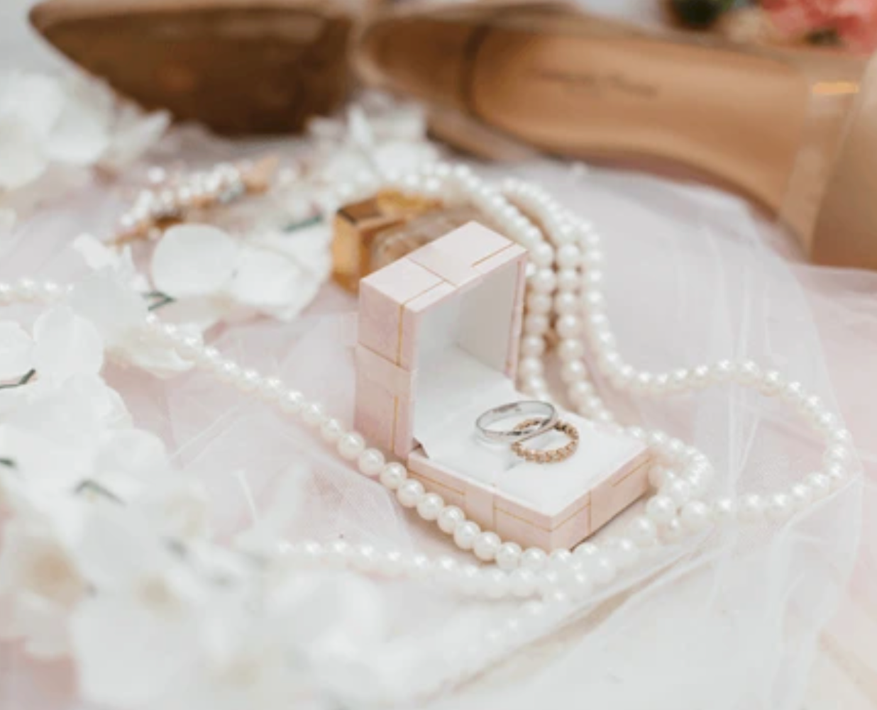 Wedding ring box with pearl necklace arranged on delicate white lace fabric.