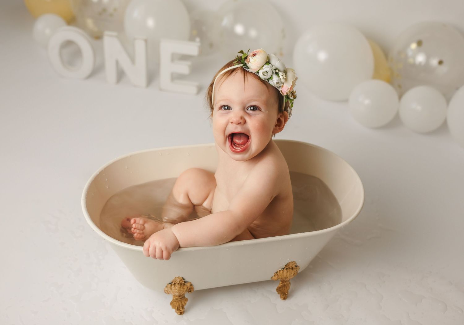 Adorable baby girl splashes in a mini tub during her first-birthday photoshoot, by Charlottesville newborn and family photographer.