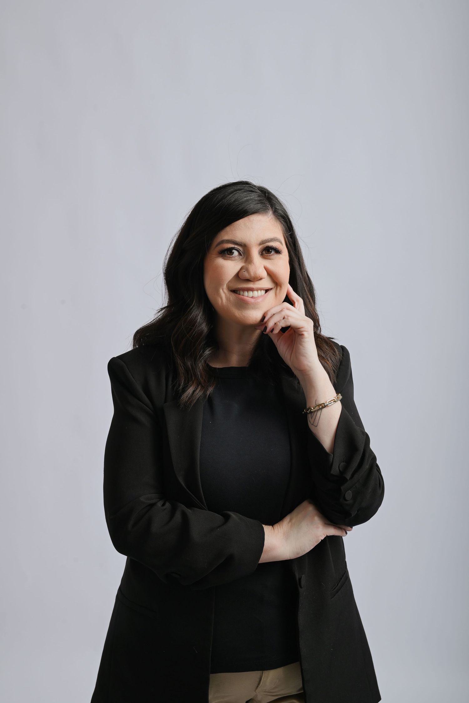 Professional portrait of someone in a black blazer and top smiling warmly against a light gray background.