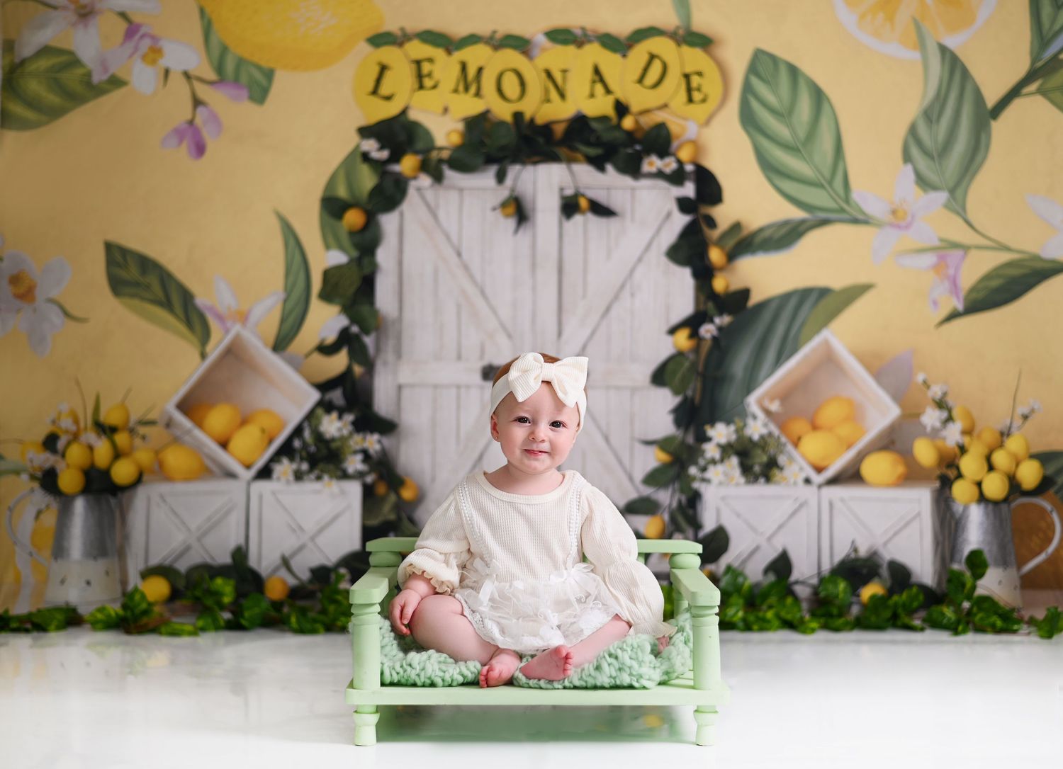 A lemonade-themed party setup with a white barn door backdrop decorated with yellow flowers and greenery.