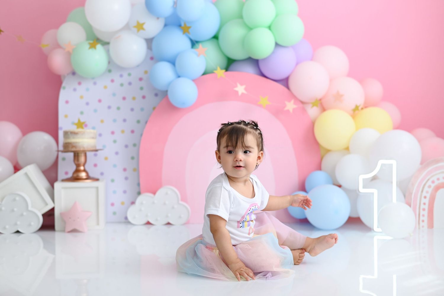Pastel balloon arch with clouds and number one decoration creates dreamy backdrop for first birthday photoshoot.