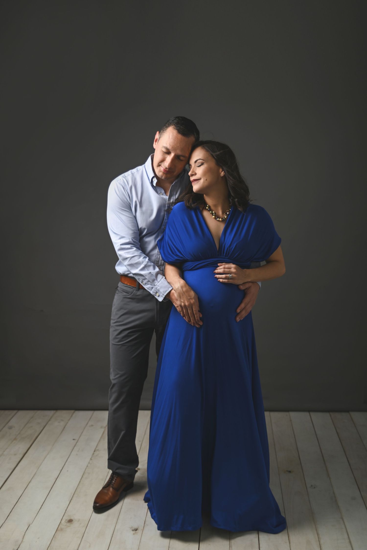 Romantic maternity portrait with couple in blue dress against dark backdrop.