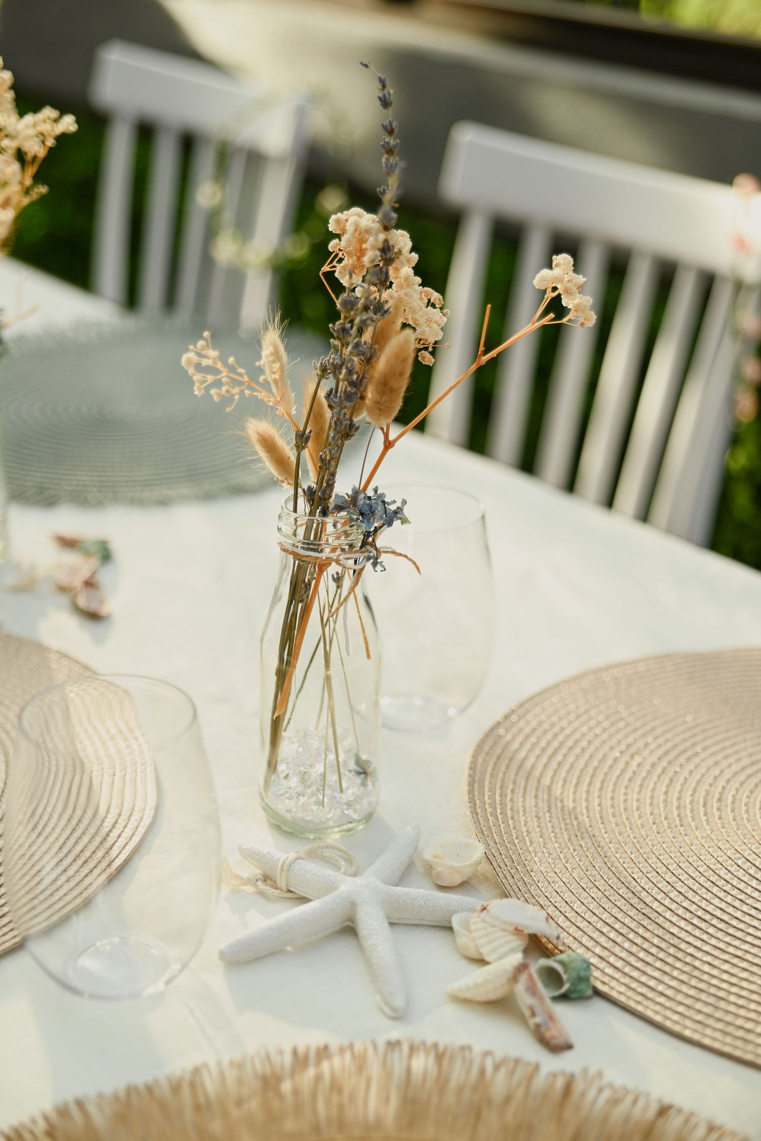 Glass vase with dried flowers on a coastal-themed table setting with starfish decor and woven placemats.