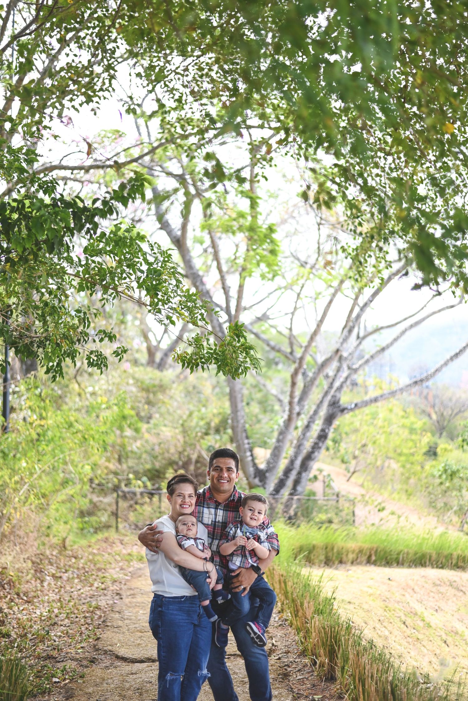 A family enjoys a sunny afternoon together on a tree-lined dirt path in a natural outdoor setting.