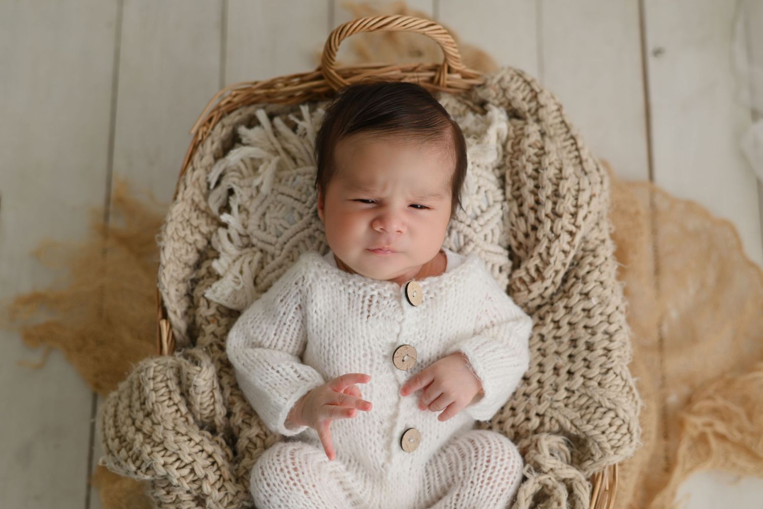 Baby wearing cozy white knit outfit rests peacefully in a beige woven basket with soft blanket.