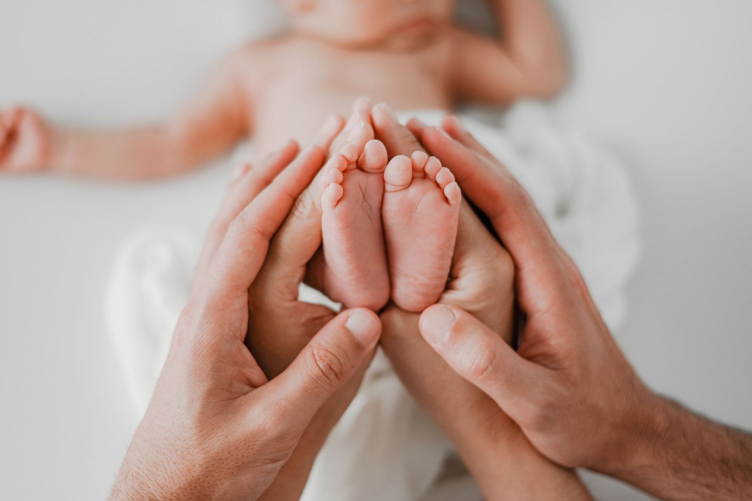 Close-up shot of tiny baby feet being gently held in adult hands against white background.