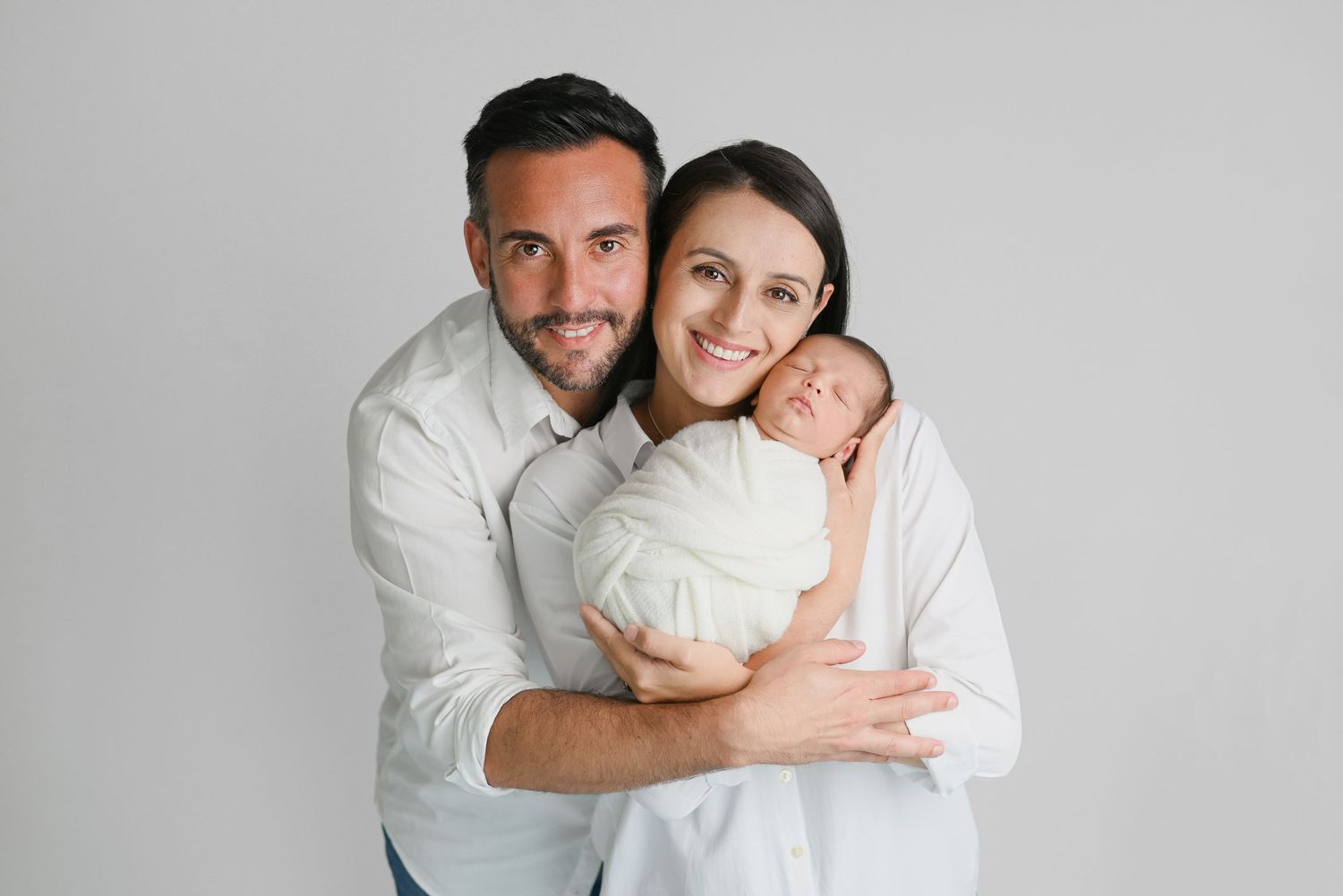 Minimalist family portrait against grey background wearing coordinated white outfits.