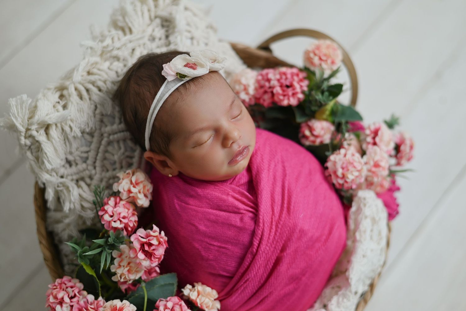 Sleeping newborn wrapped in bright pink swaddle nestled among pink carnations and white lace.