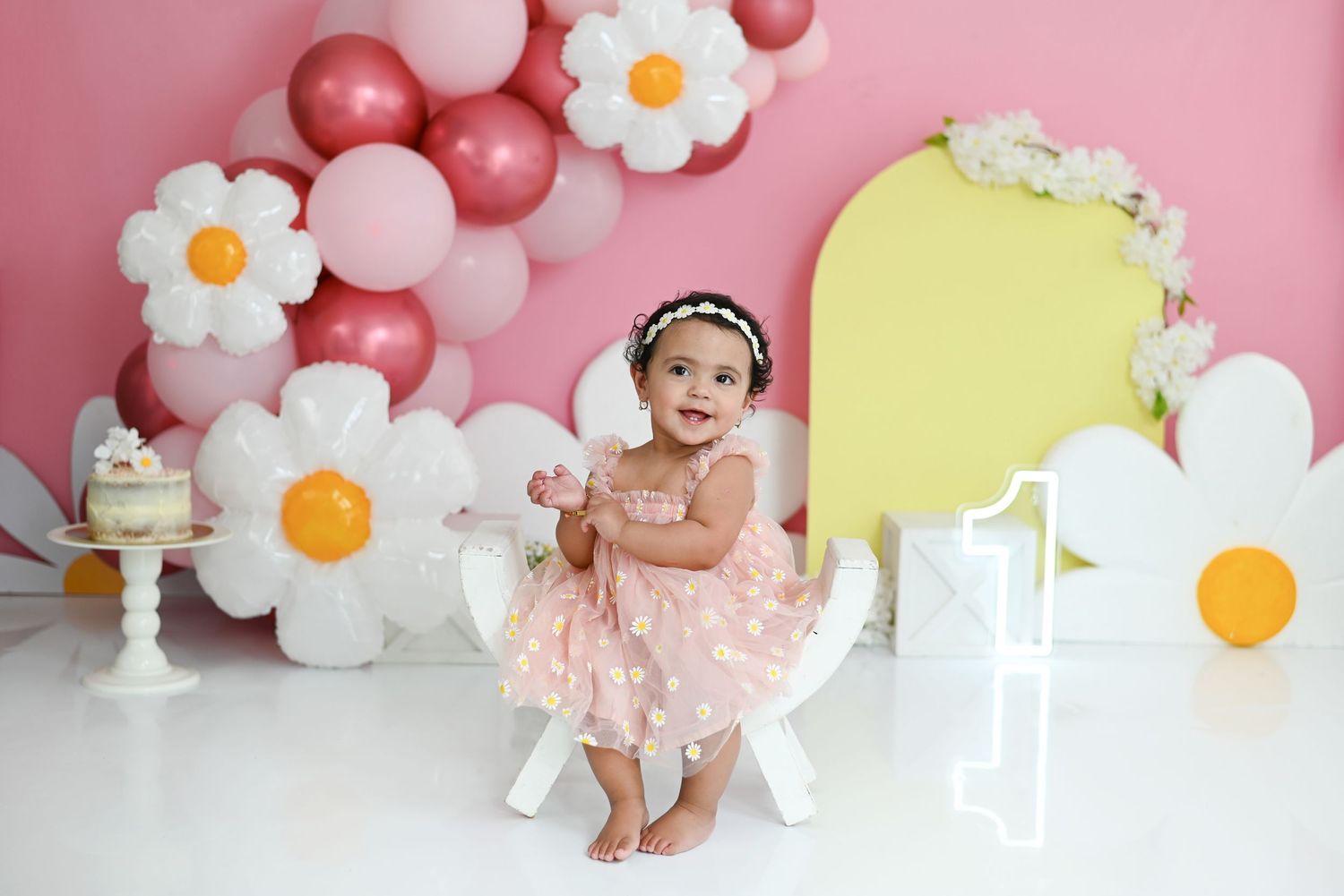 Pink floral backdrop with white daisy decorations and balloons for a birthday photoshoot setup.
