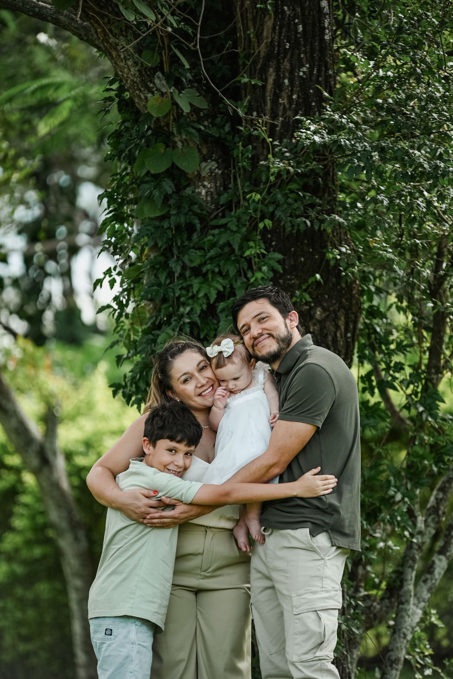 A loving family shares a warm embrace outdoors surrounded by lush green foliage on a sunny day.