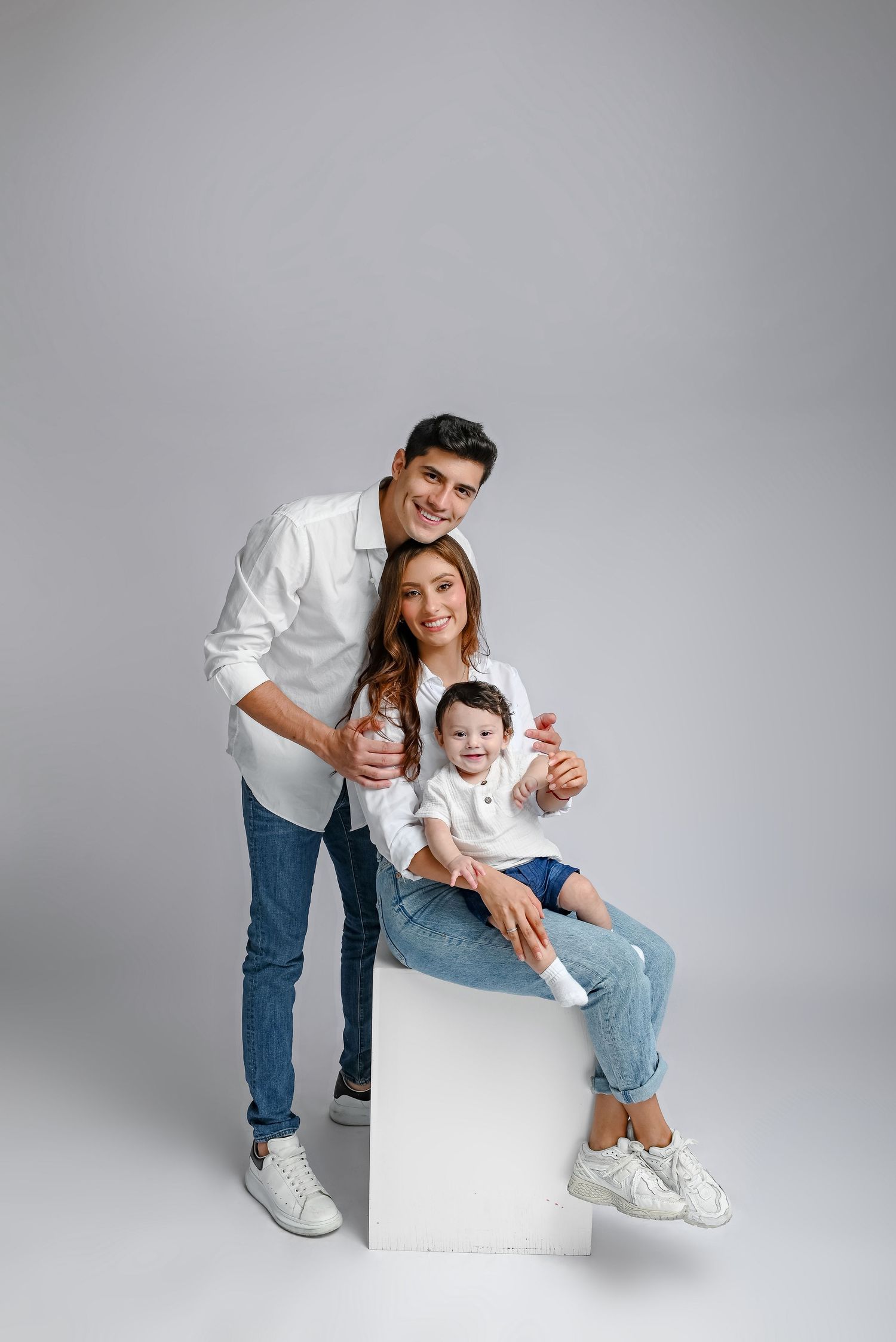 A joyful family portrait in casual attire posing together against a gray studio background.