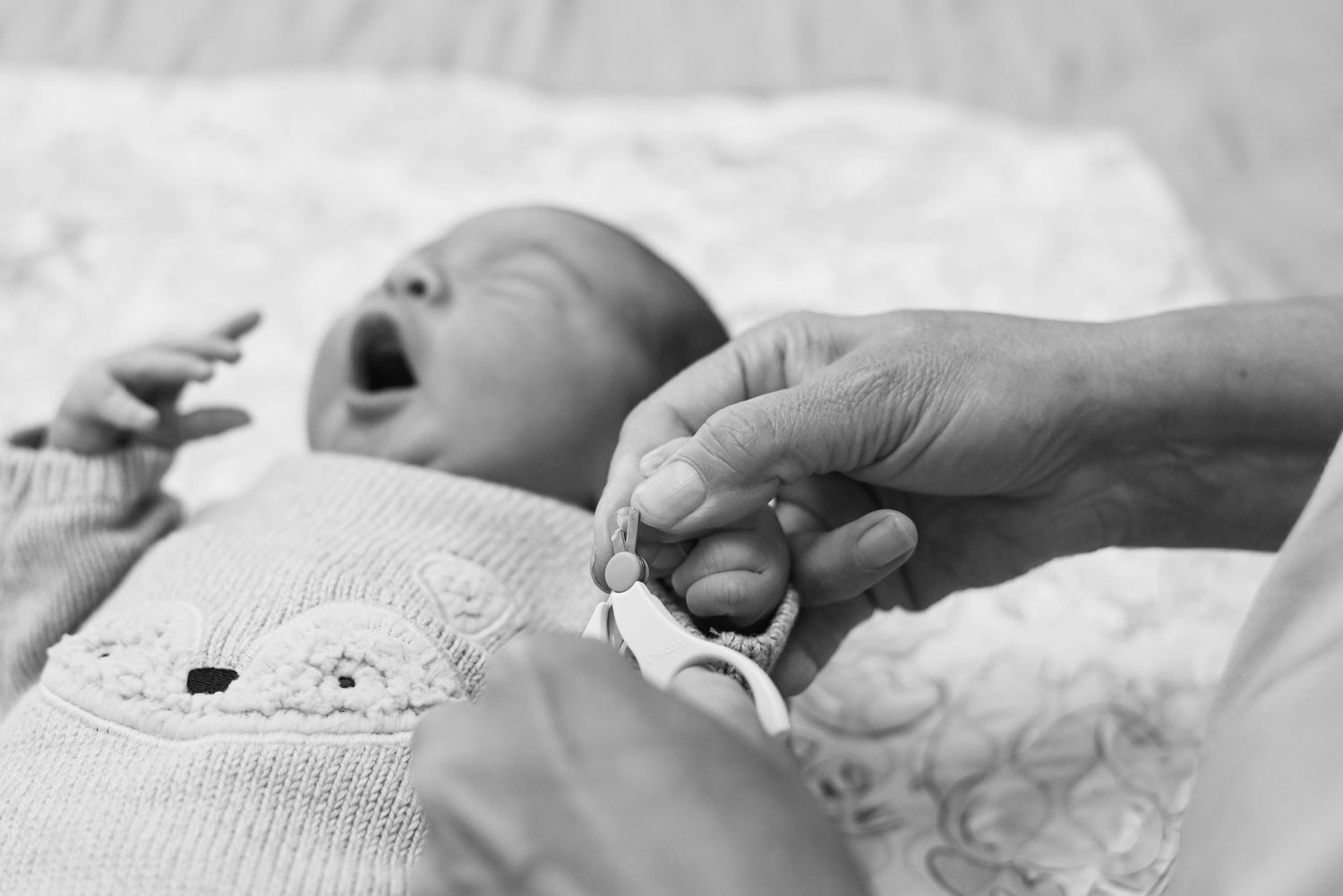 Black and white image of tiny newborn baby hand grasping adult finger while lying on white blanket.